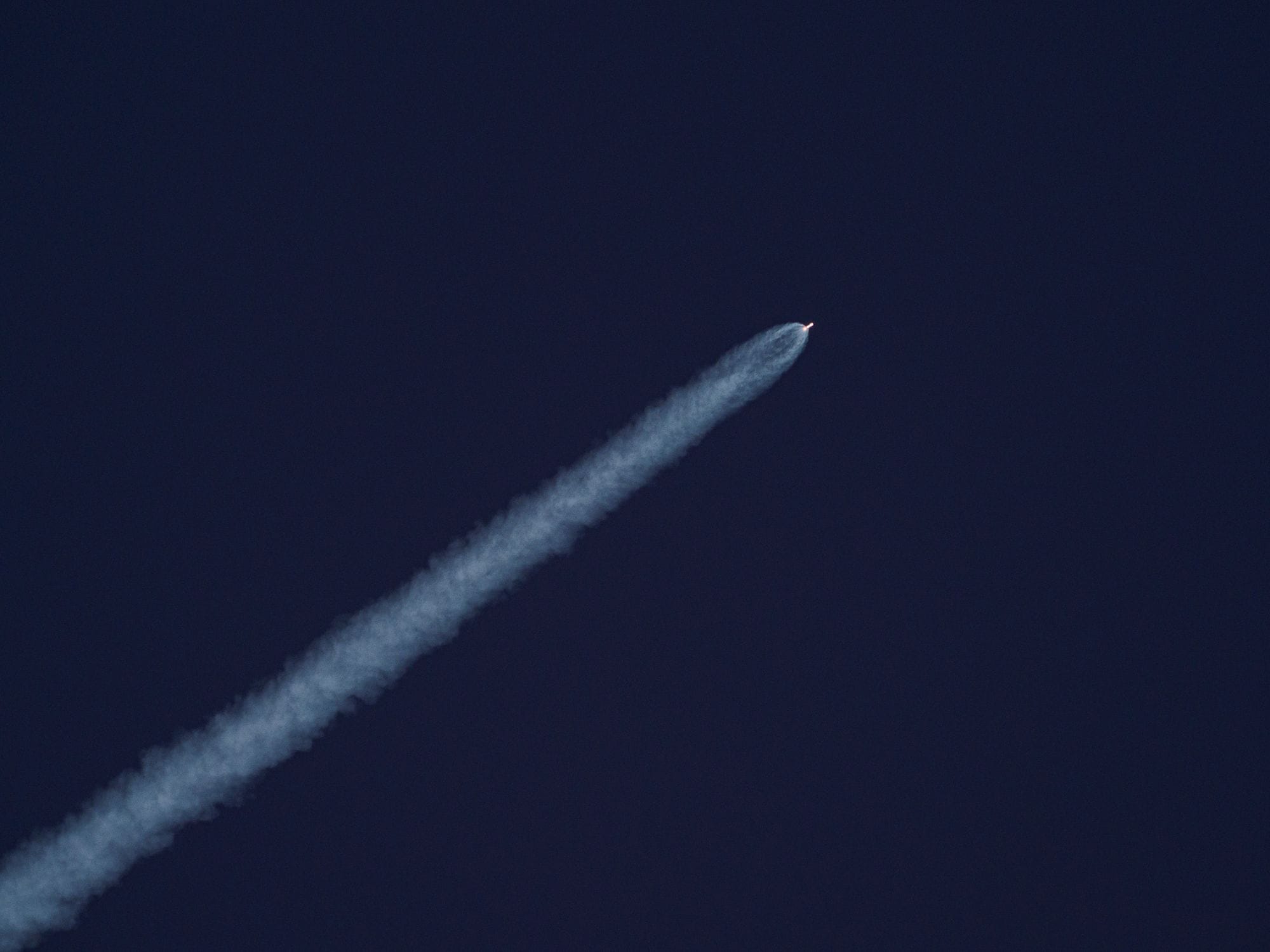 A rocket ascends into the sky, leaving a trail of smoke against the clear blue sky.