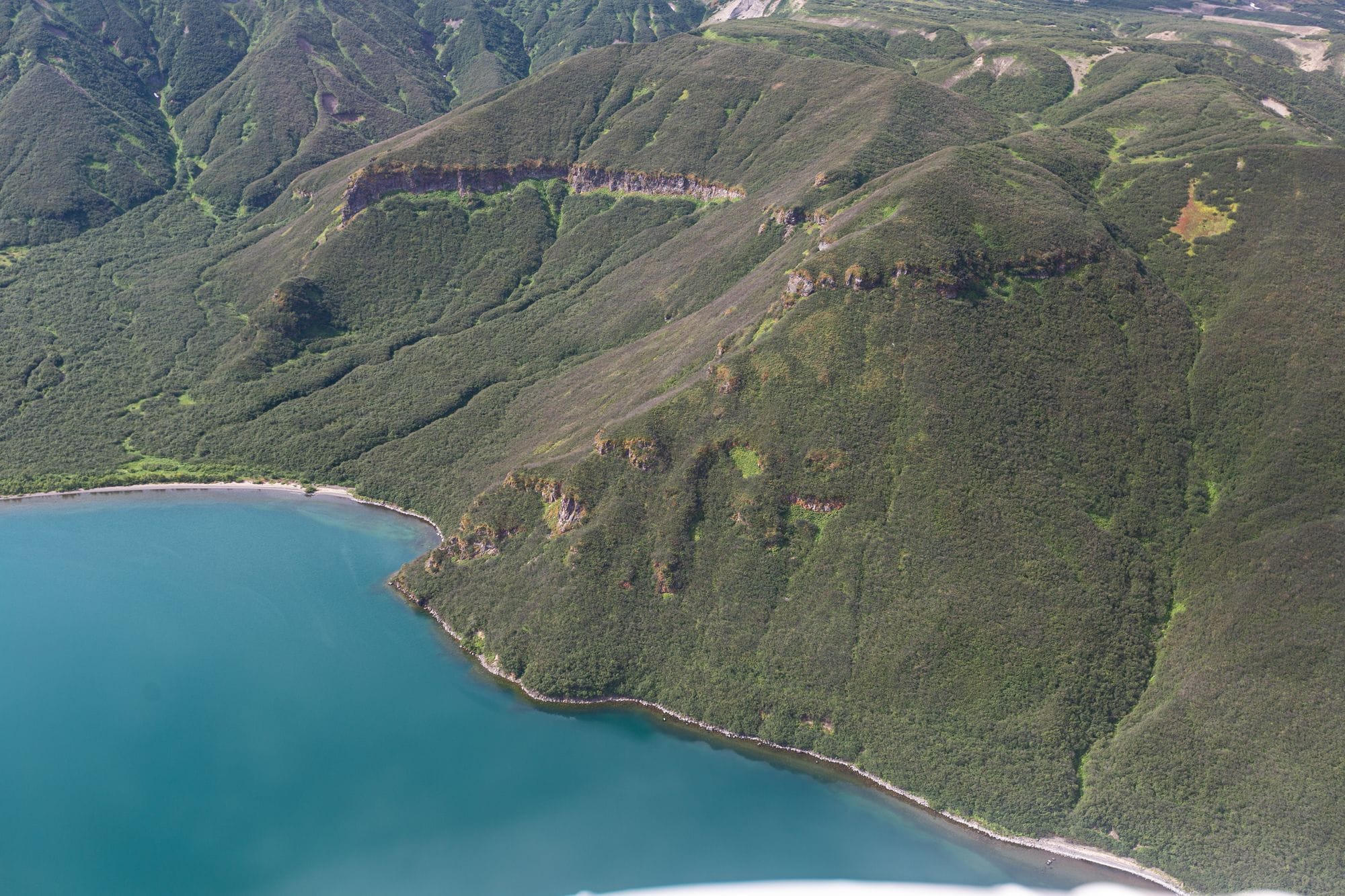 A stunning aerial view of a green mountain range beside a serene coastline.