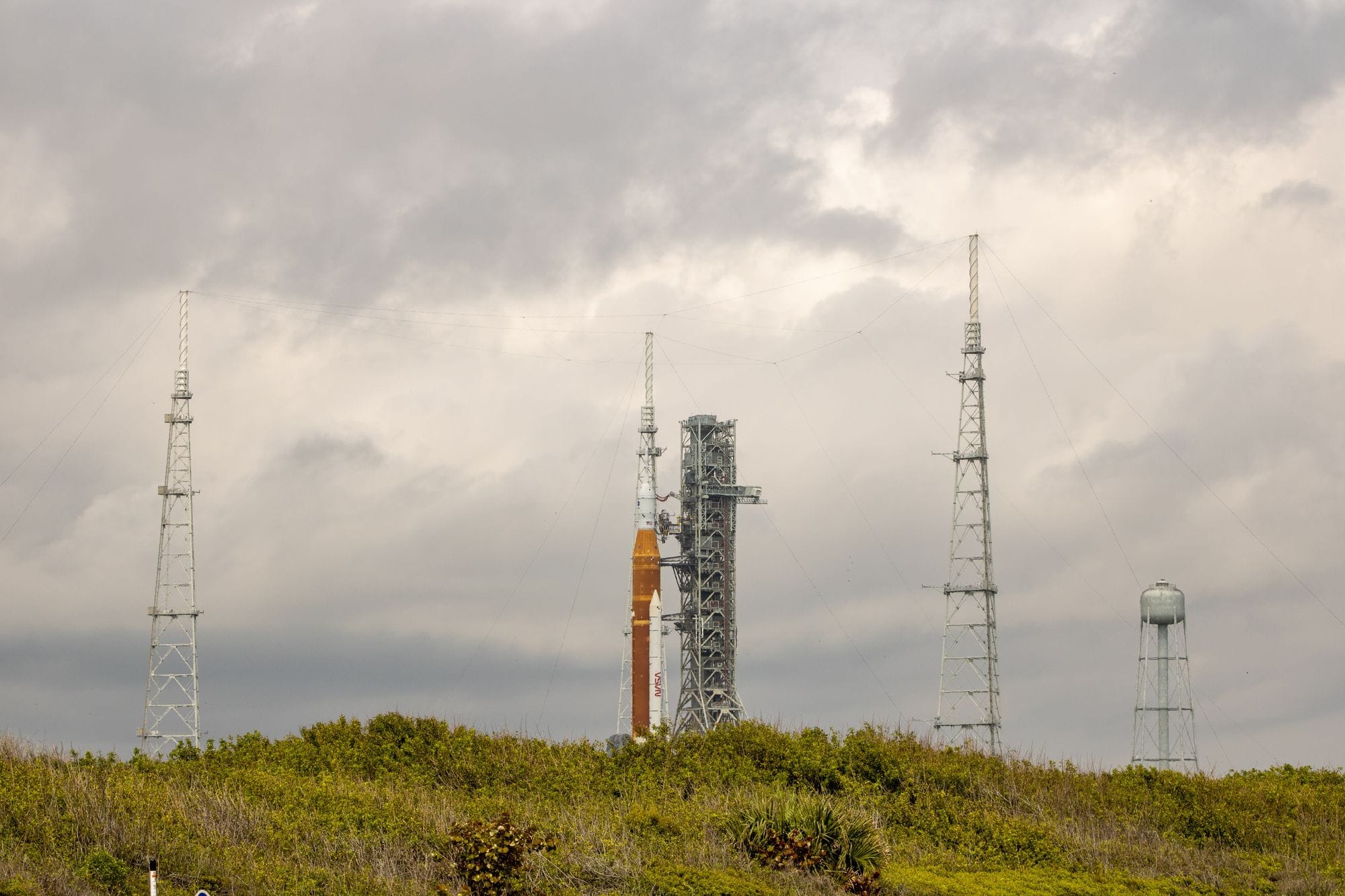 NASA rocket on launch pad surrounded by antennas against a cloudy sky.