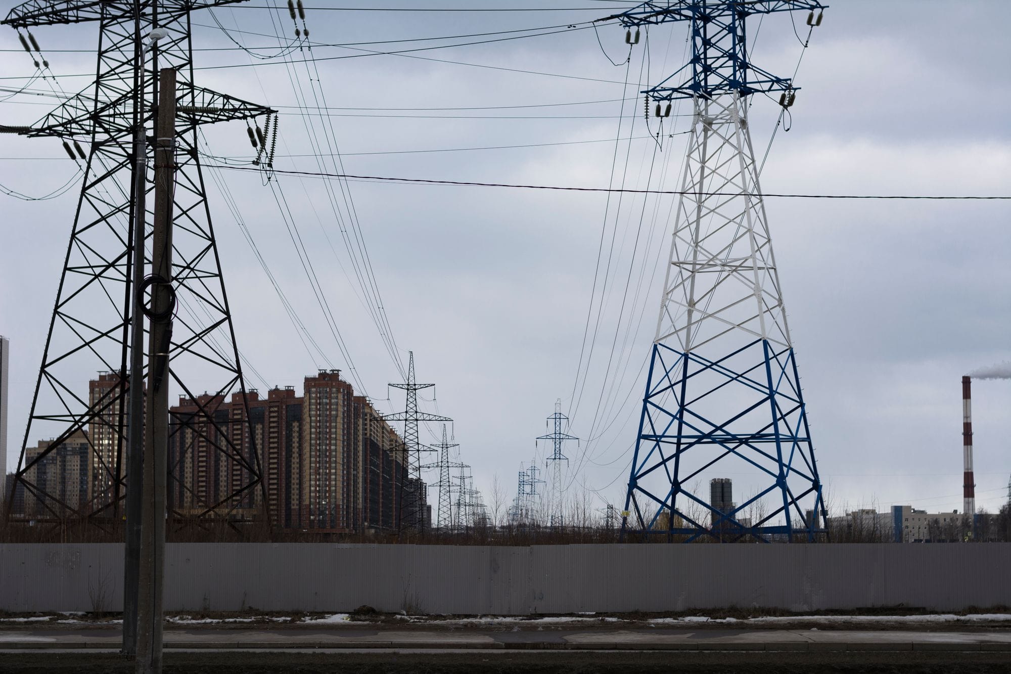 Cityscape featuring electricity pylons against a cloudy sky.