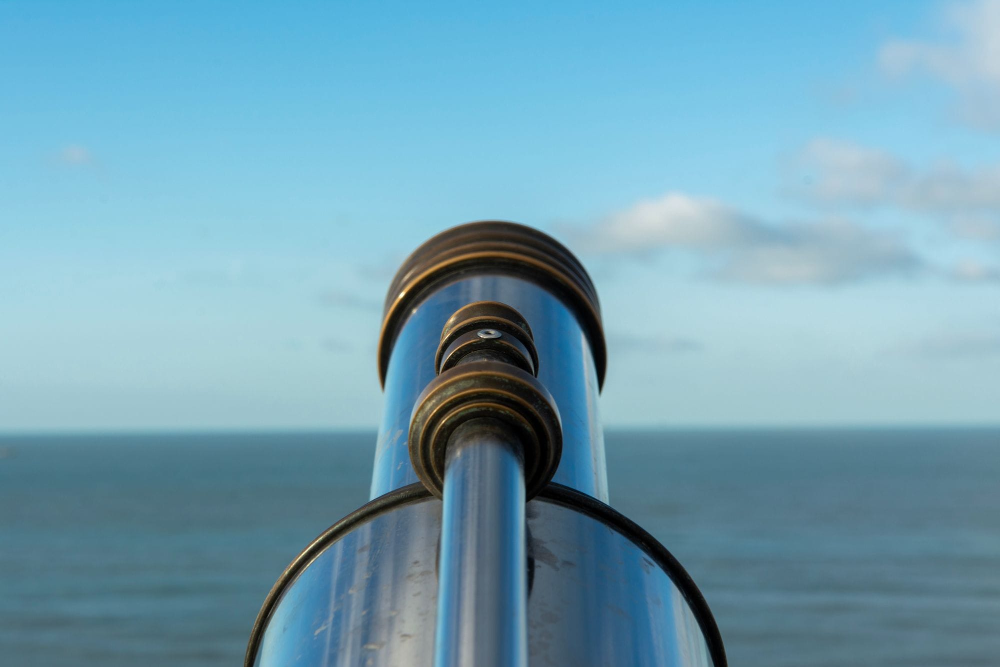 A shiny telescope facing a vast ocean under a clear blue sky, perfect for beachside observation.