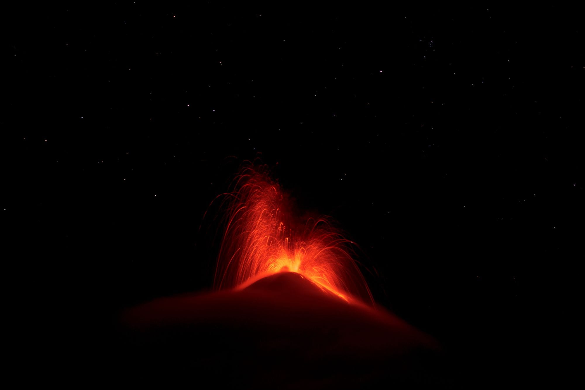 Spectacular volcano eruption at night under a starry sky, capturing fiery lava and ash plumes against the darkness.