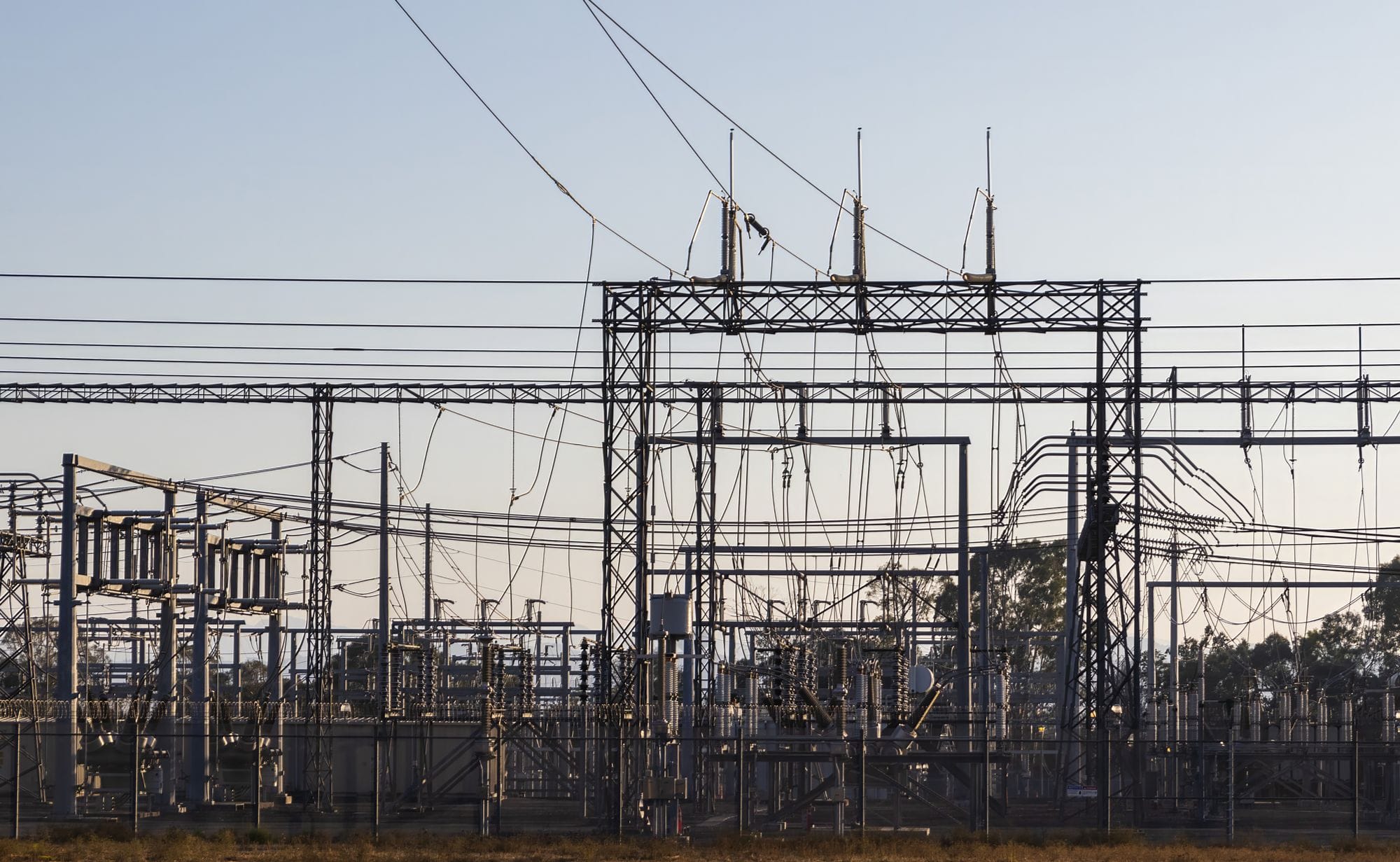 High-voltage electrical substation with steel structures and power lines at dawn.