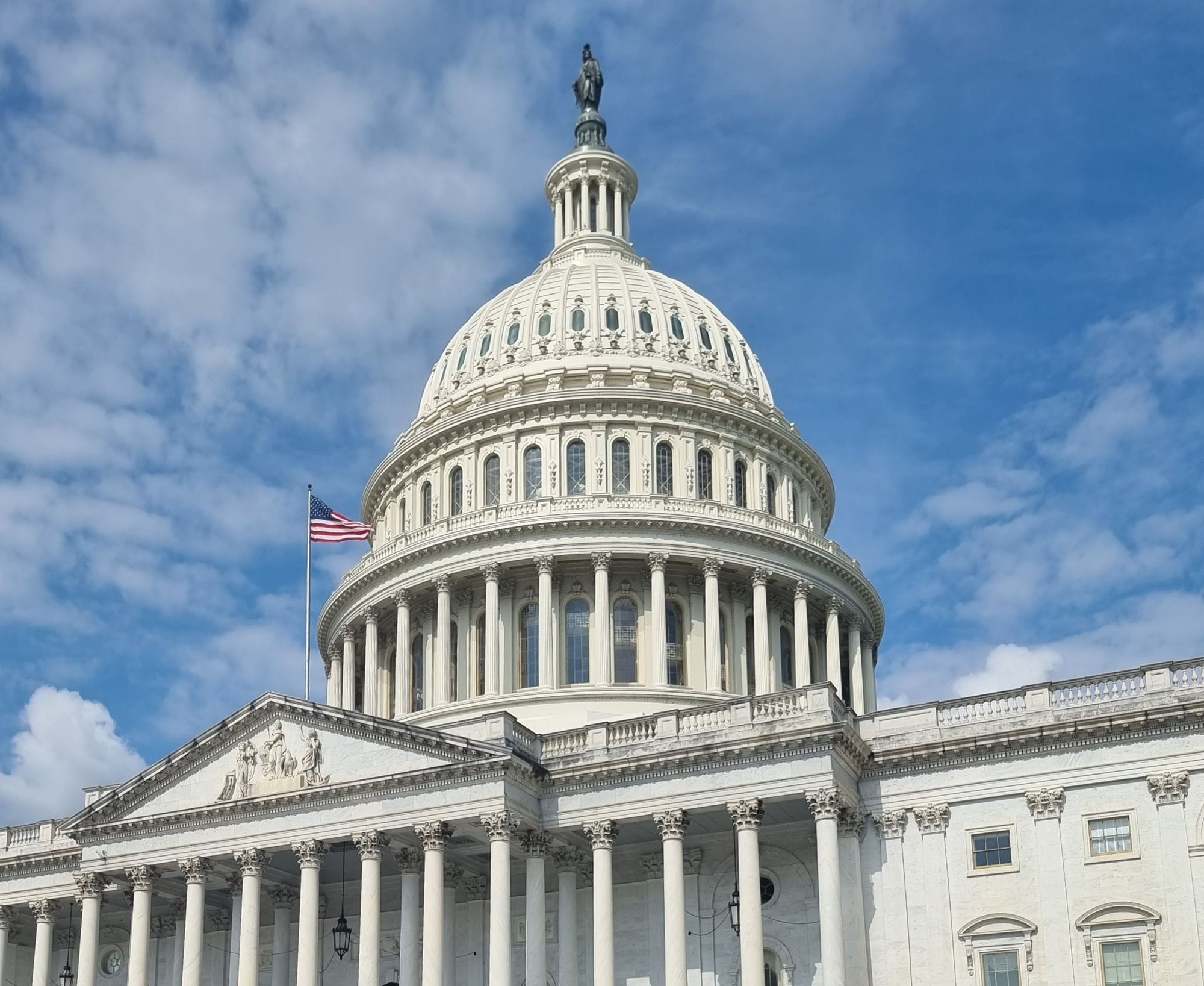 A striking view of the US Capitol dome with flag and blue sky in Washington, DC.