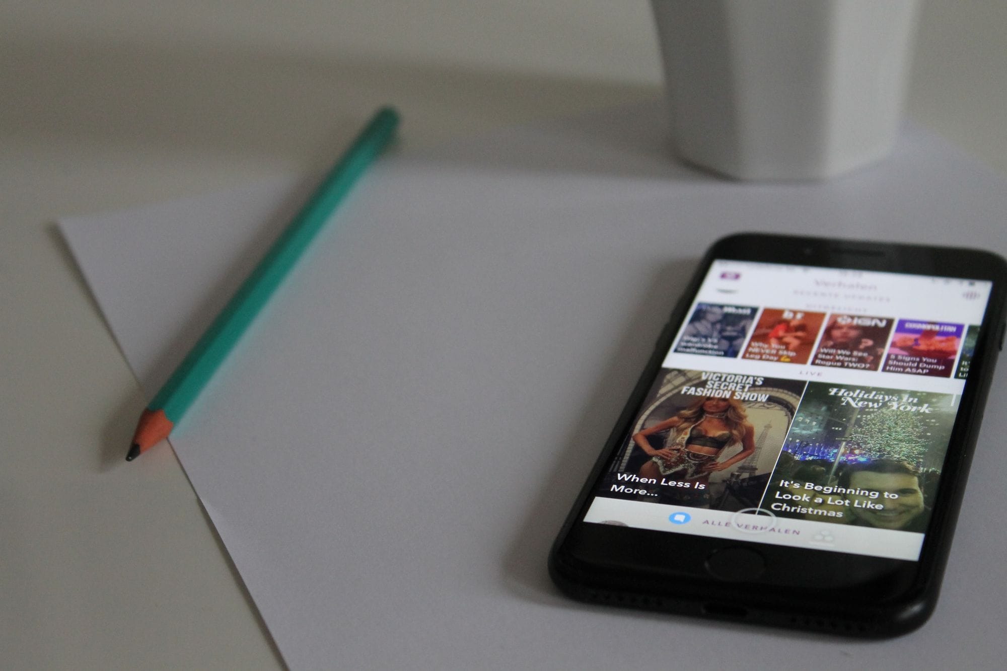 Smartphone displaying news, next to pencil and paper on a desk, showcasing modern technology in a workspace.