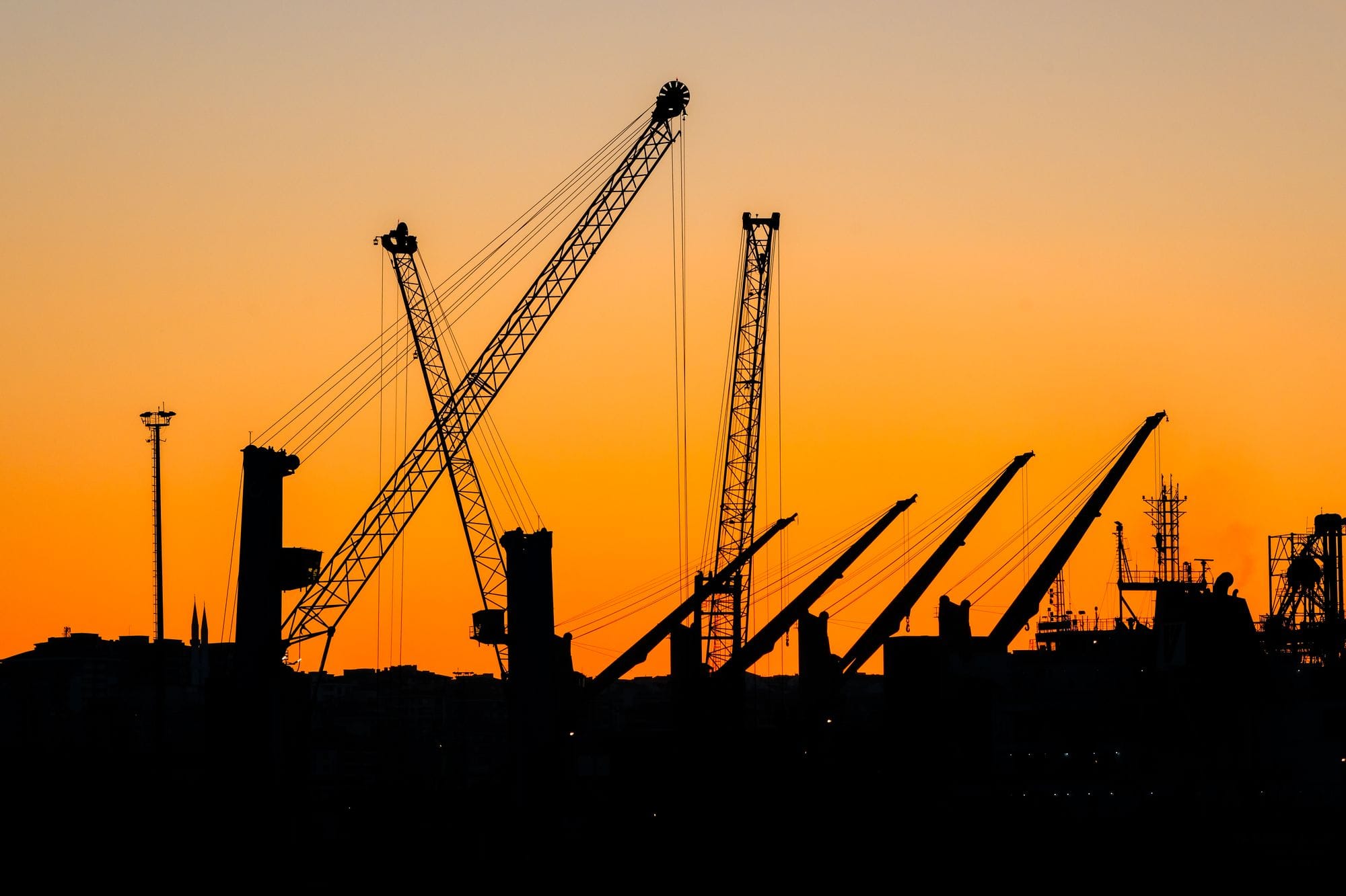 Silhouette of industrial cranes against a vibrant sunset skyline. Ideal for urban and industrial themes.