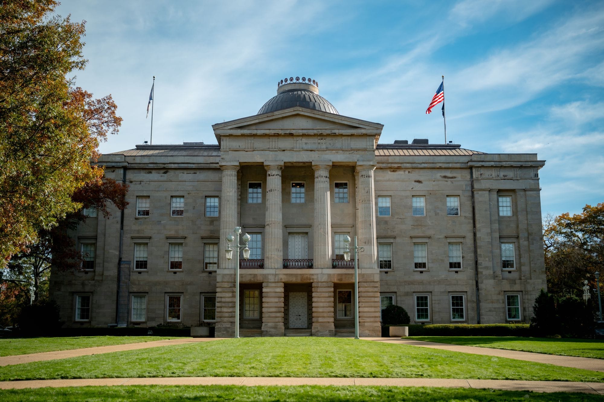 Front view of the historic North Carolina State Capitol in Raleigh, showcasing neoclassical architecture under a blue sky.