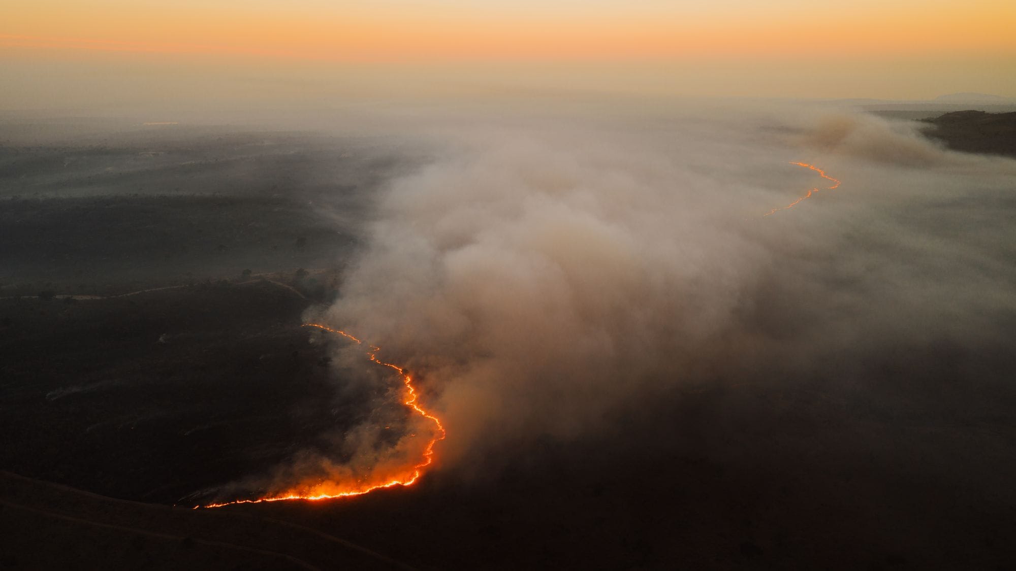 Dramatic aerial shot of a forest fire spreading with smoke at sunset in South Africa.
