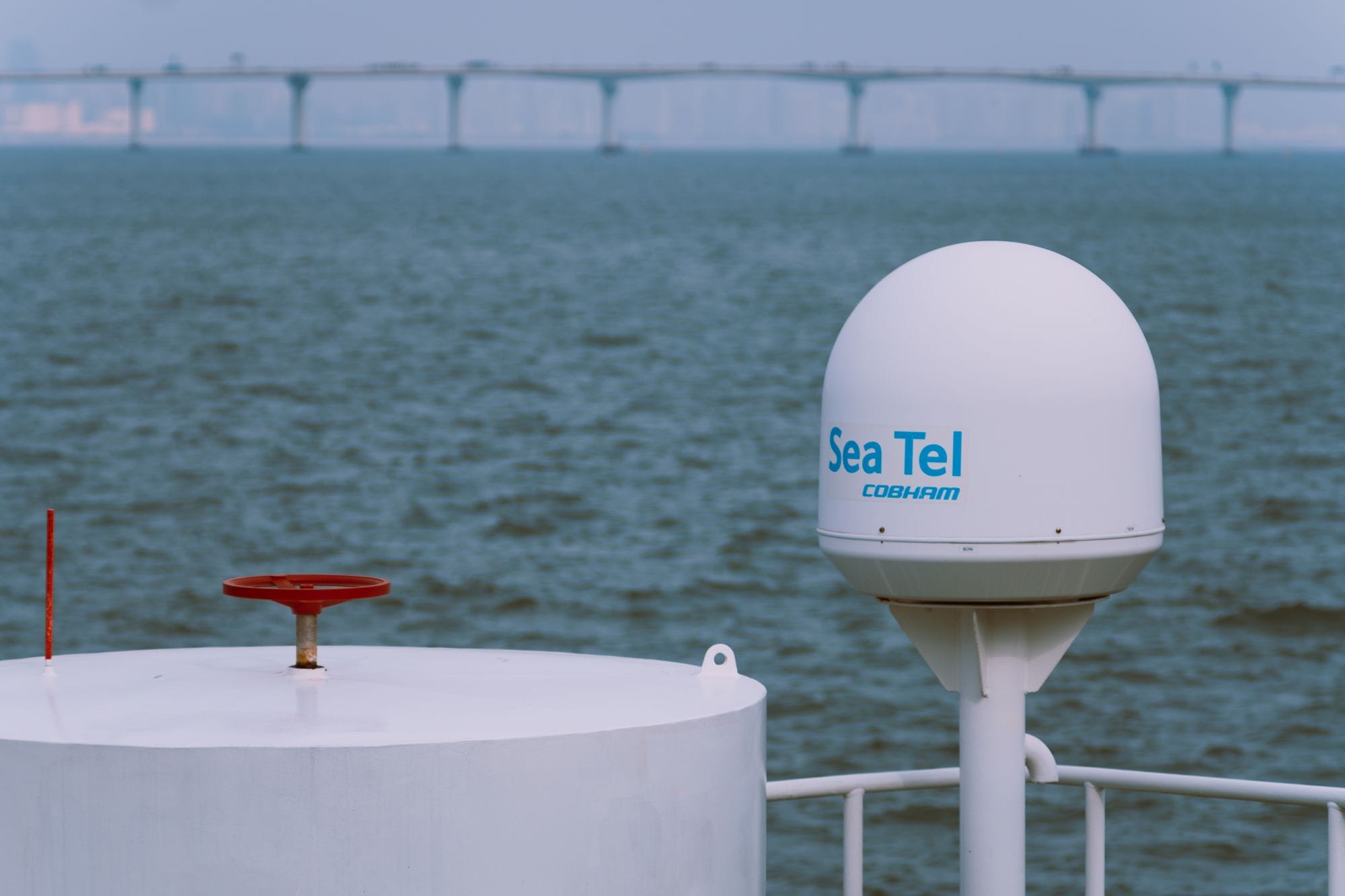 A Sea Tel satellite antenna on a vessel with a bridge in the background over the ocean.
