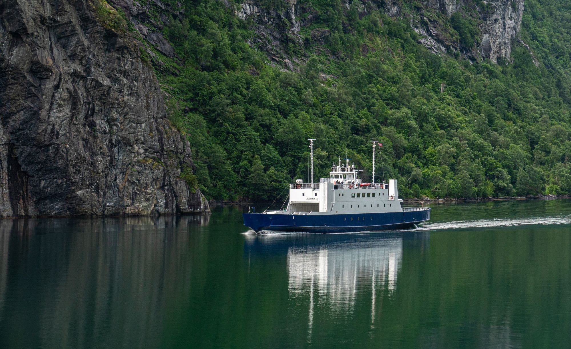 A ferry sailing through the serene waters of a Norwegian fjord with lush green mountains.