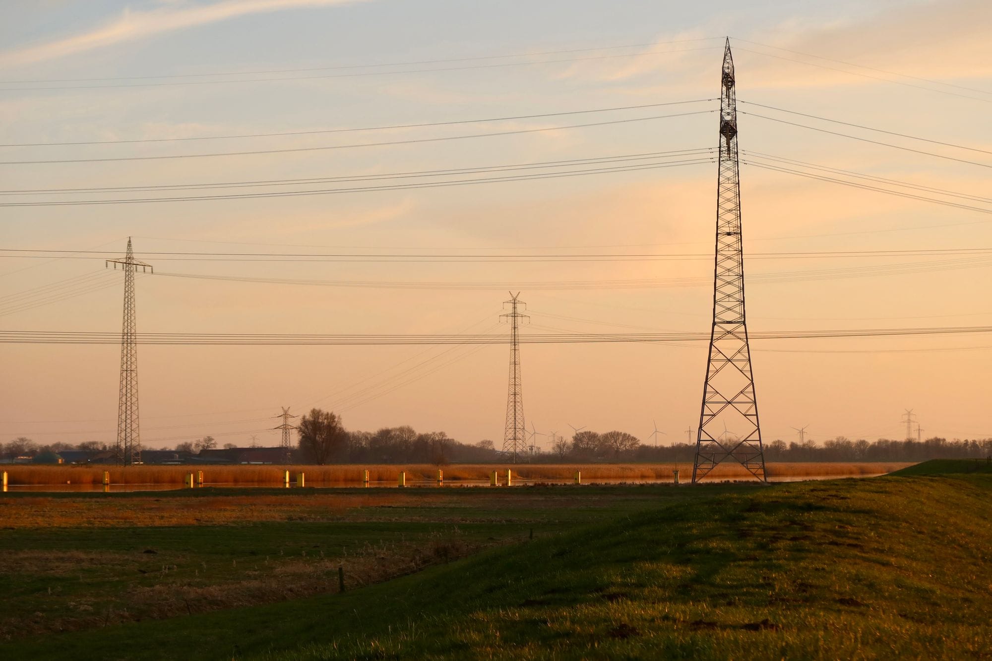 Power lines stretch across a rural landscape at sunset, creating a serene and industrial scene.