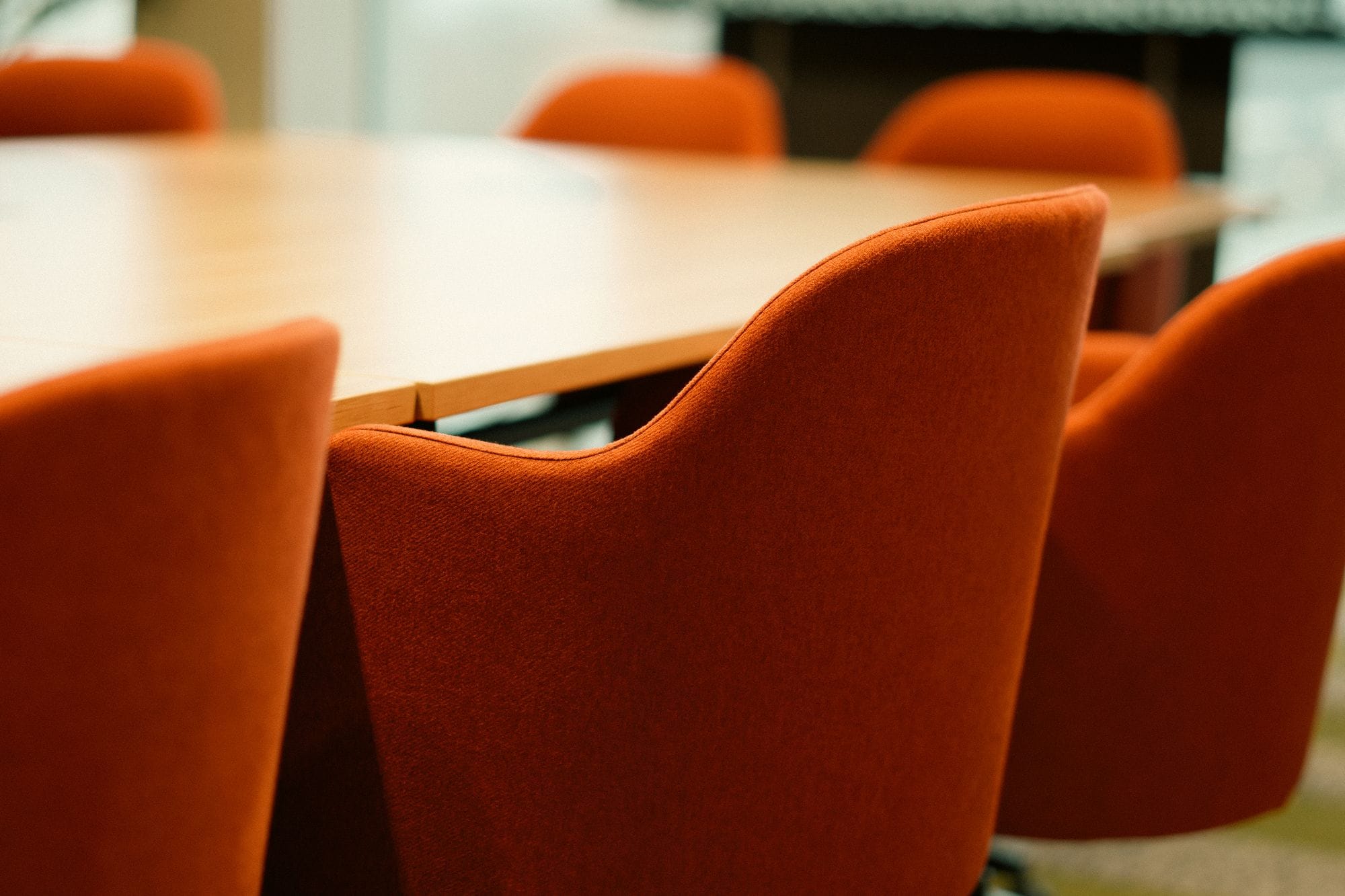 Close-up view of modern orange chairs around a conference table in an office setting.