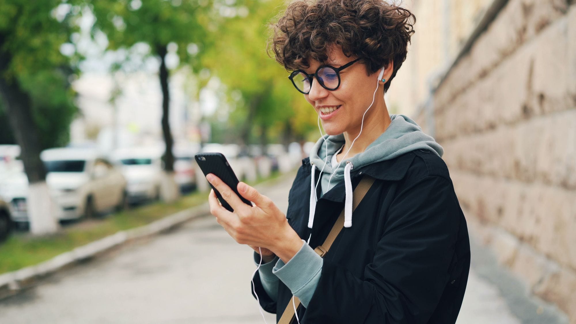 Young person enjoying music on smartphone outdoors, smiling.