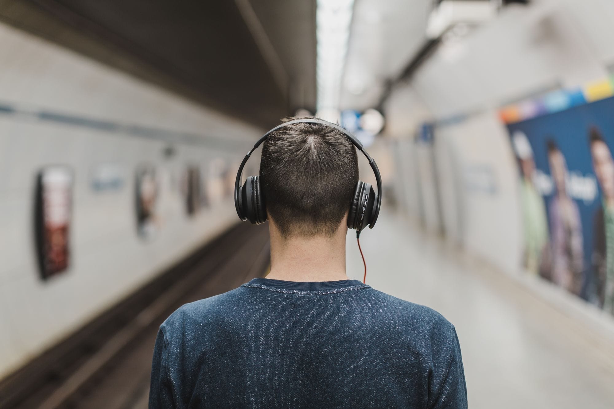 Rear view of a young man listening to music with headphones at a subway platform.