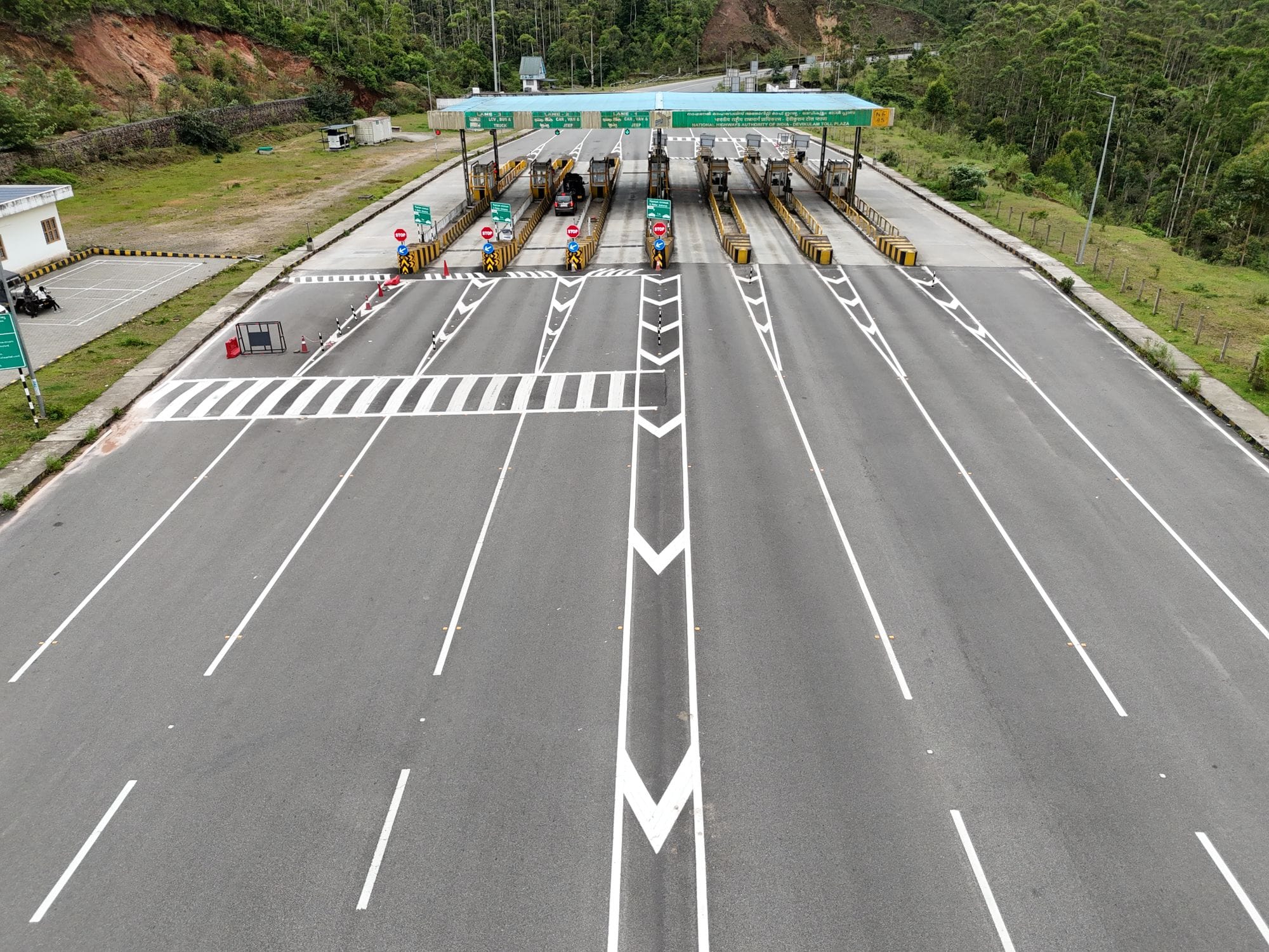 Aerial shot of an empty multi-lane toll booth on a highway surrounded by greenery.
