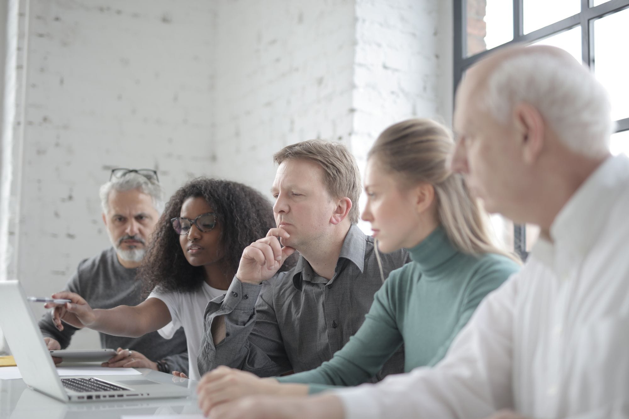 African American female employee pointing with pen at netbook screen while talking about project to diverse serious colleagues sitting in light office