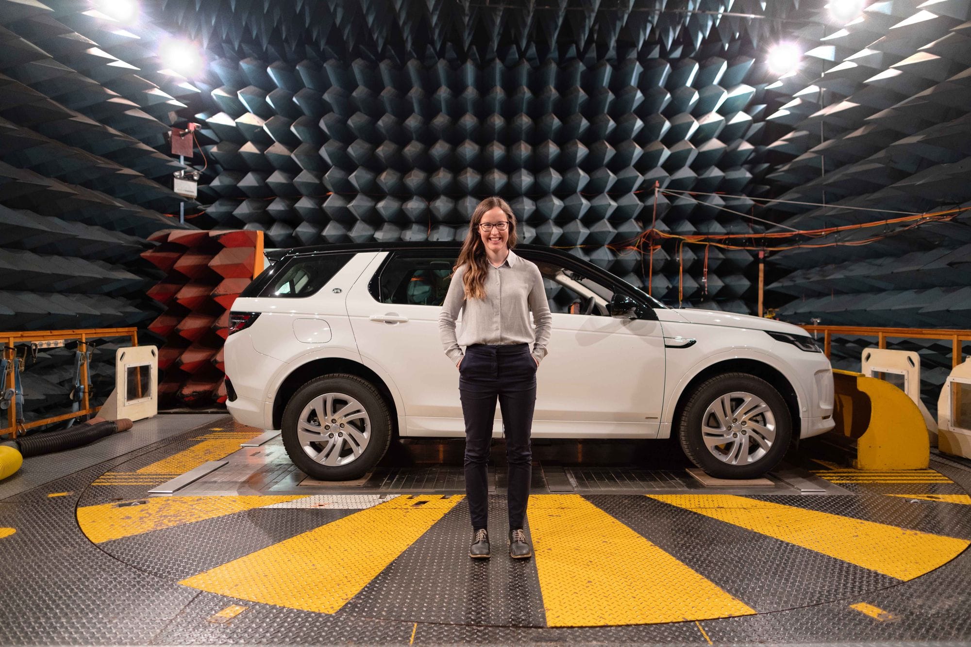 Female engineer stands in anechoic chamber with a car for sound testing.