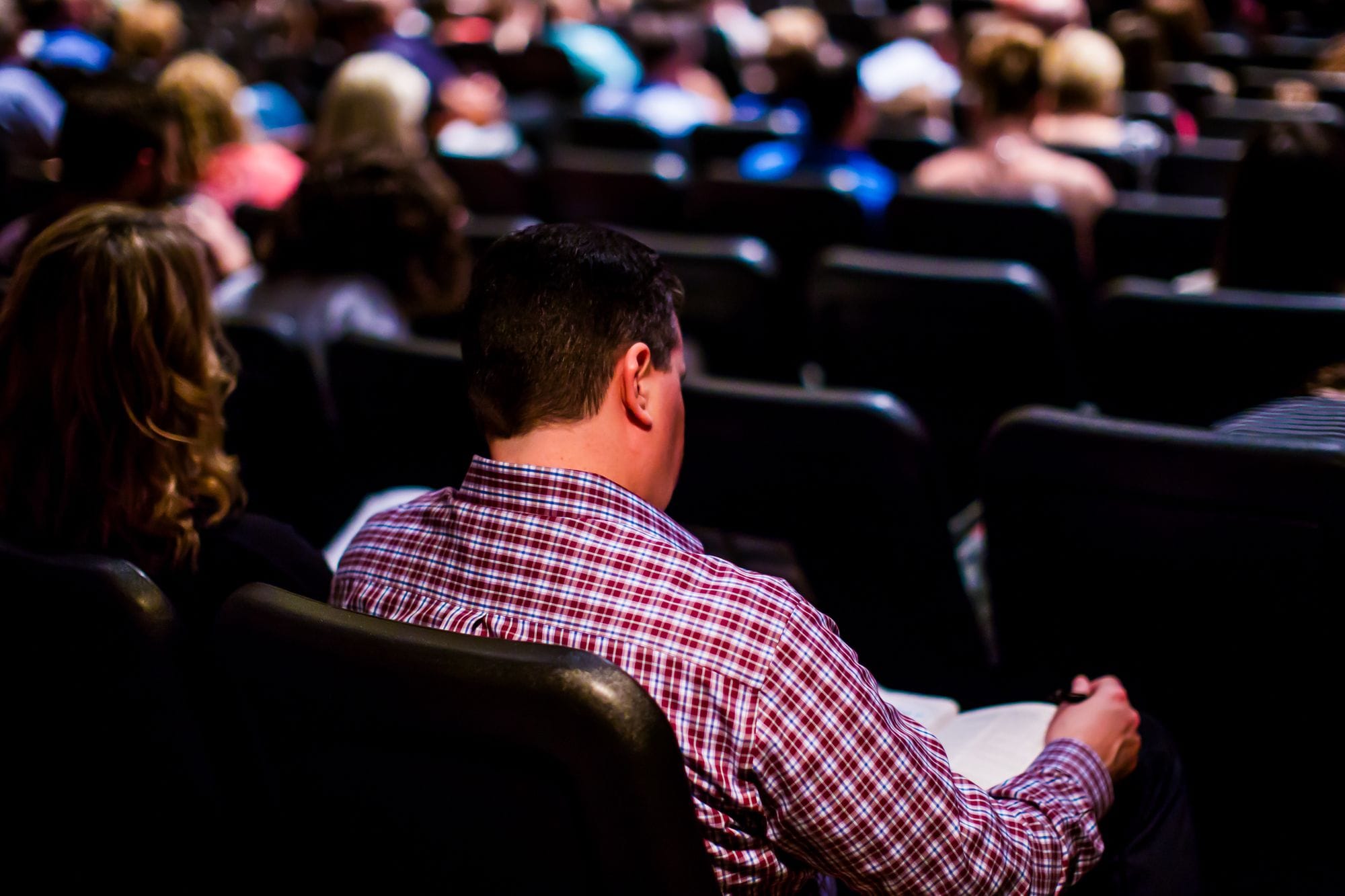 View of an audience in a lecture hall with focus on an individual writing notes.