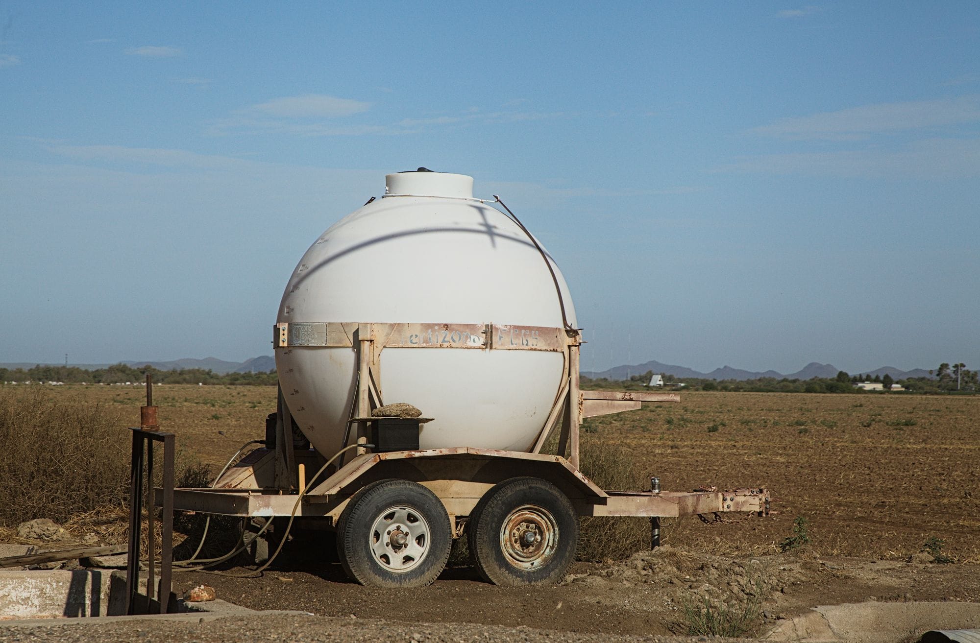 A round water tank on a trailer set in a rural field under a clear blue sky.