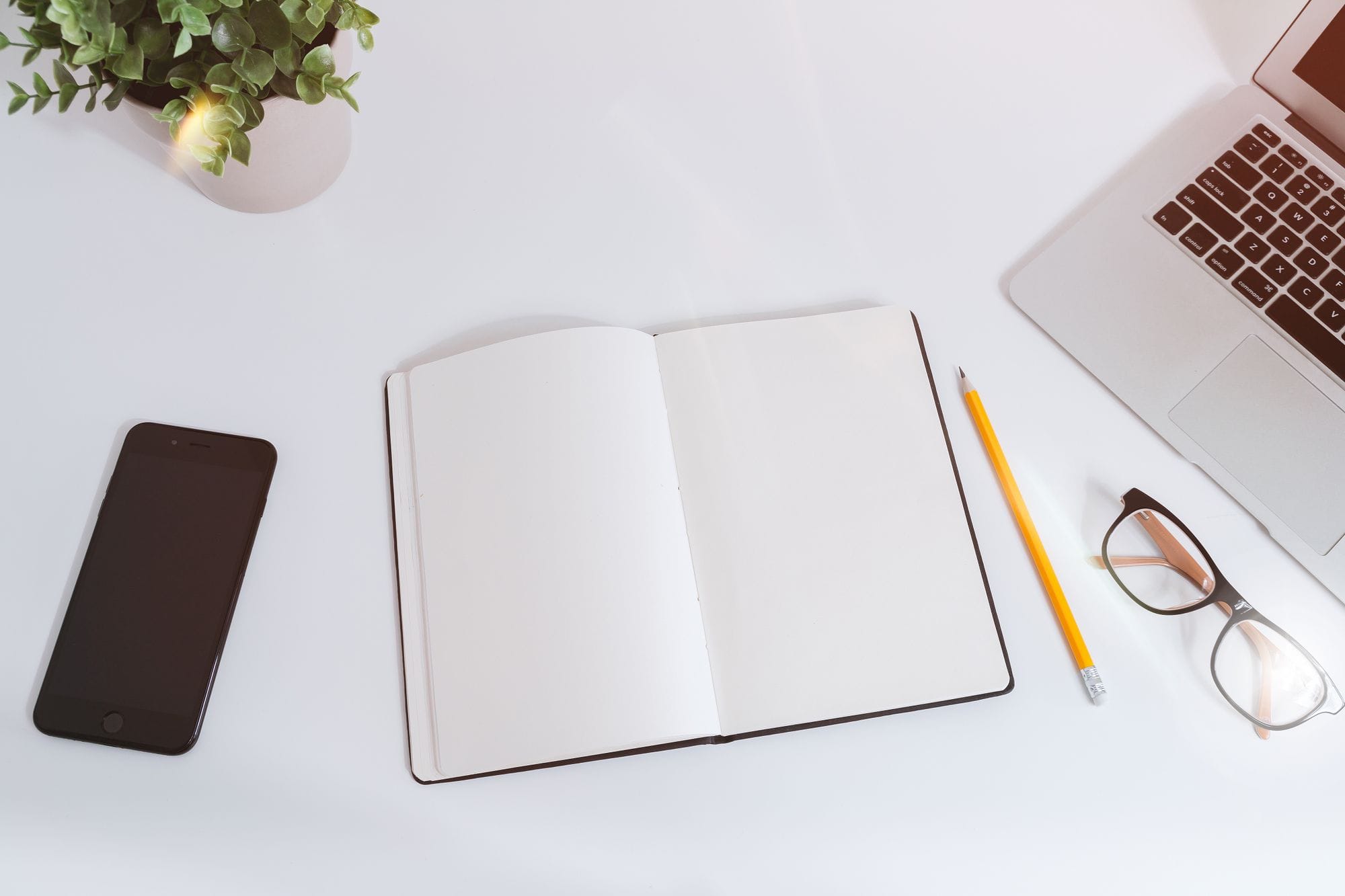 An organized workspace with a notebook, smartphone, and laptop on a bright, clean desk.
