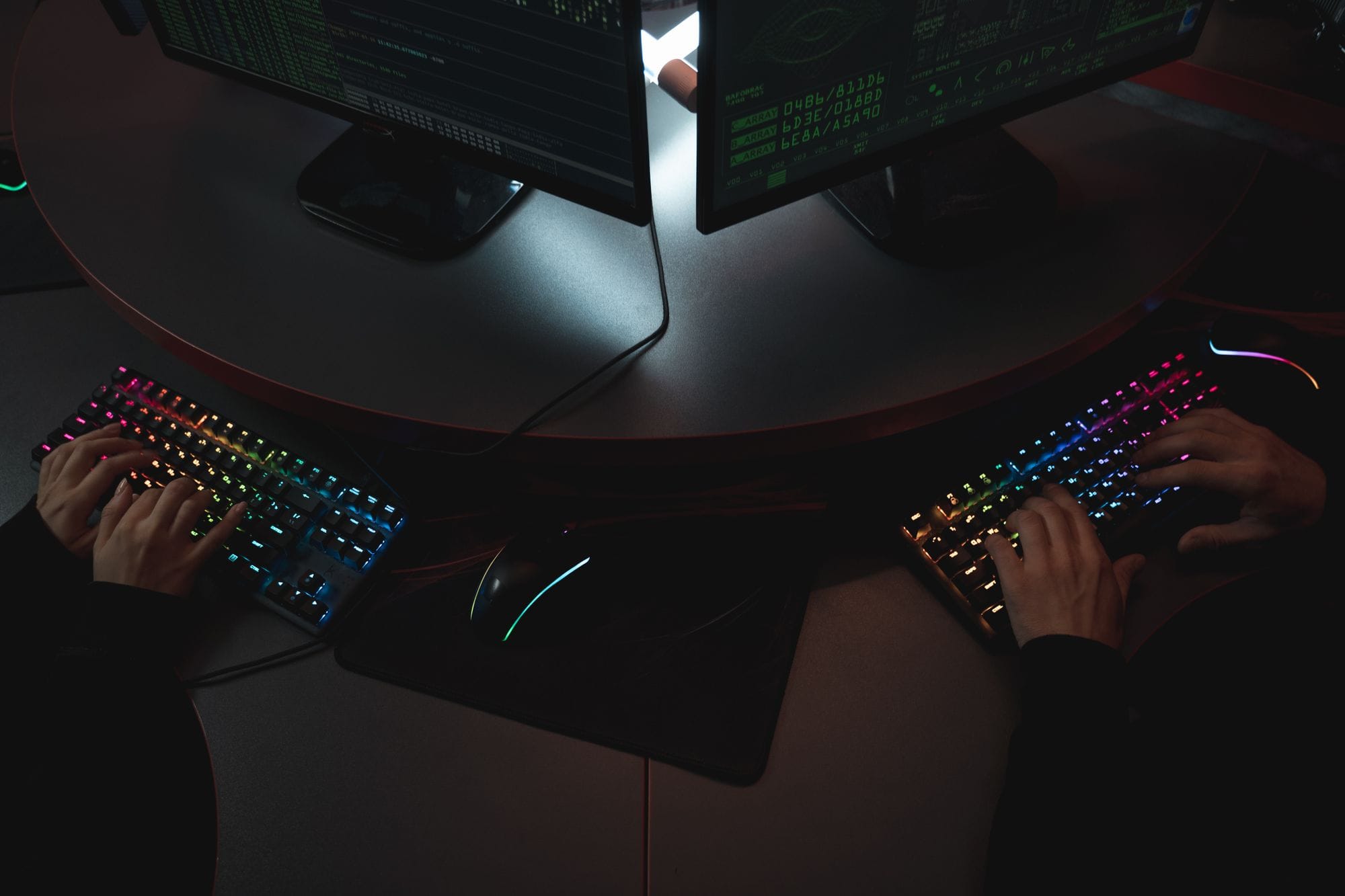 Two people typing on RGB keyboards with code on screens, indicating a cybersecurity environment.