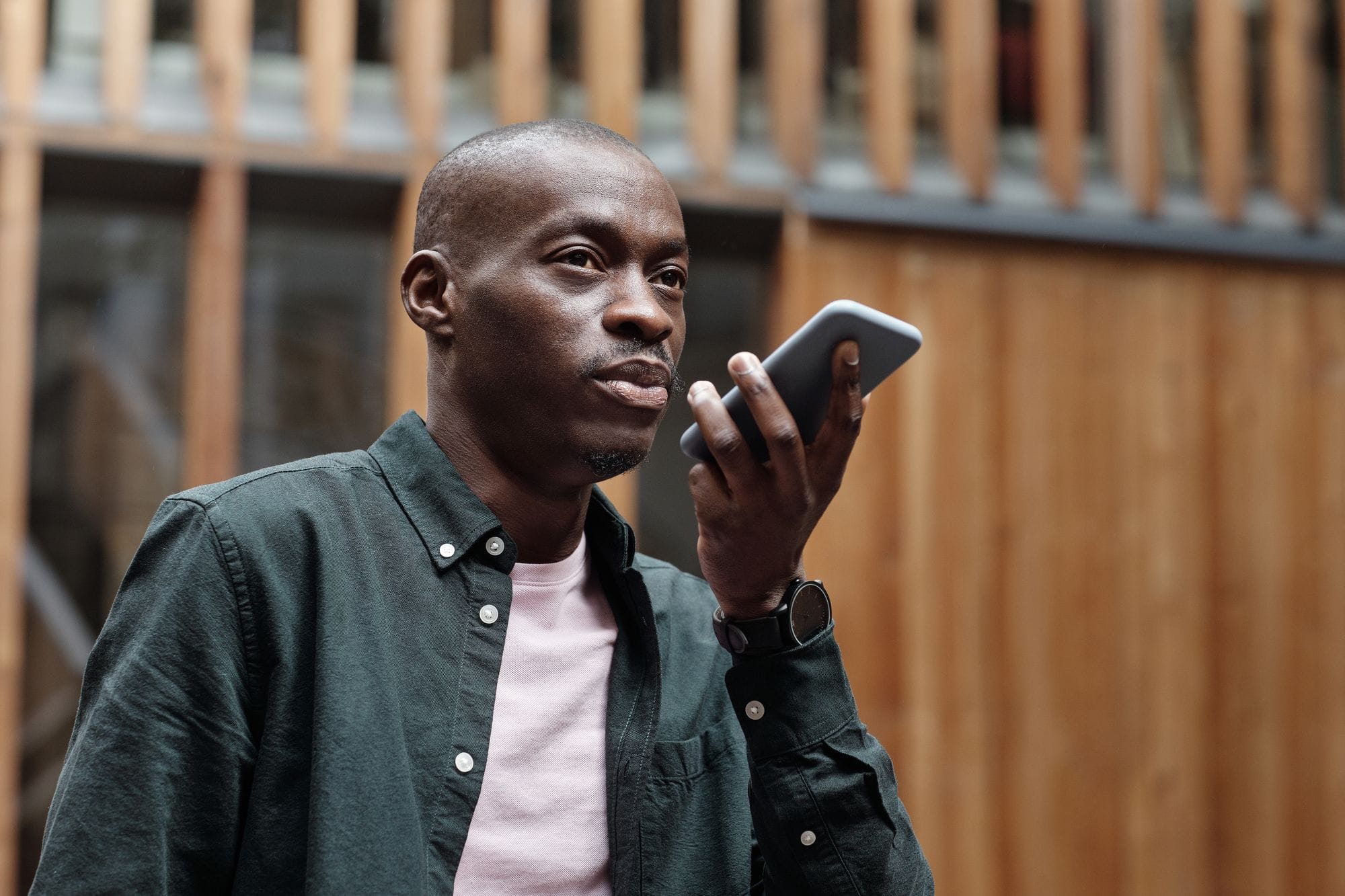 Stylish adult man using his smartphone for voice commands in an outdoor urban setting.