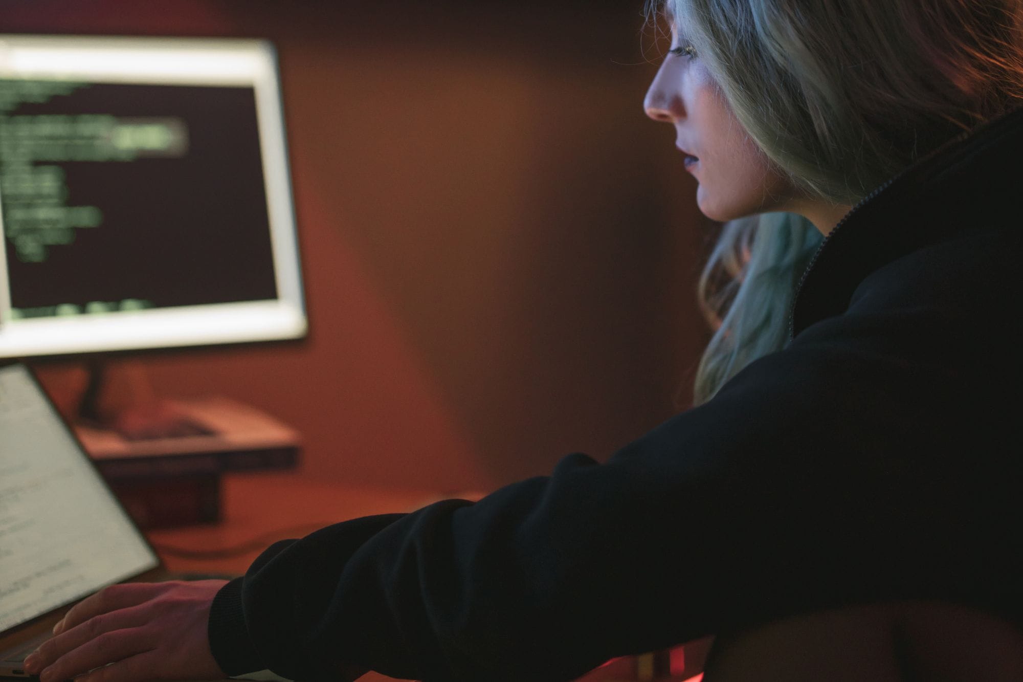 A woman working late on a laptop with code displayed on the screen in a dark room.
