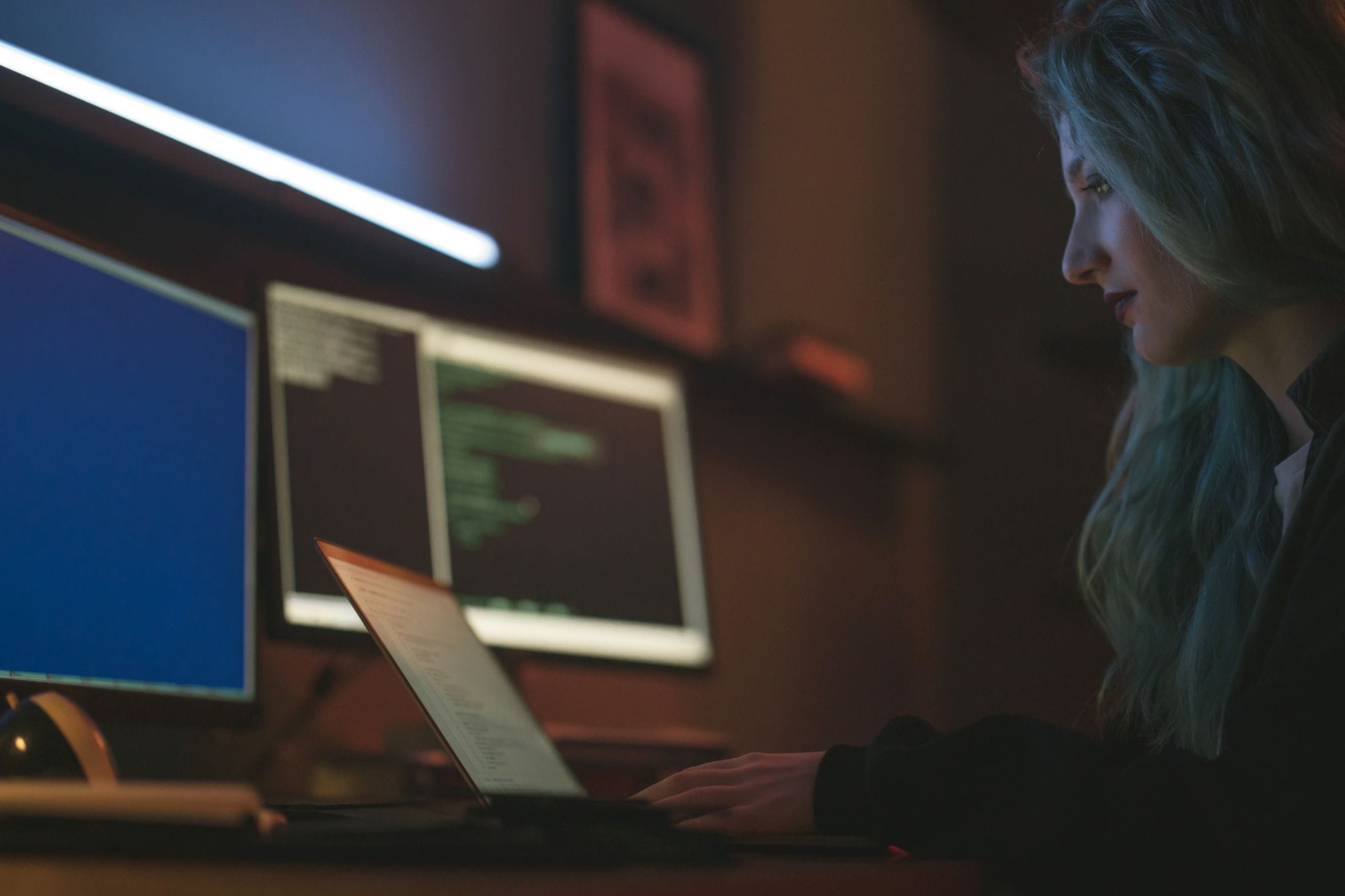 Woman working on cybersecurity programming with laptops and multiple screens