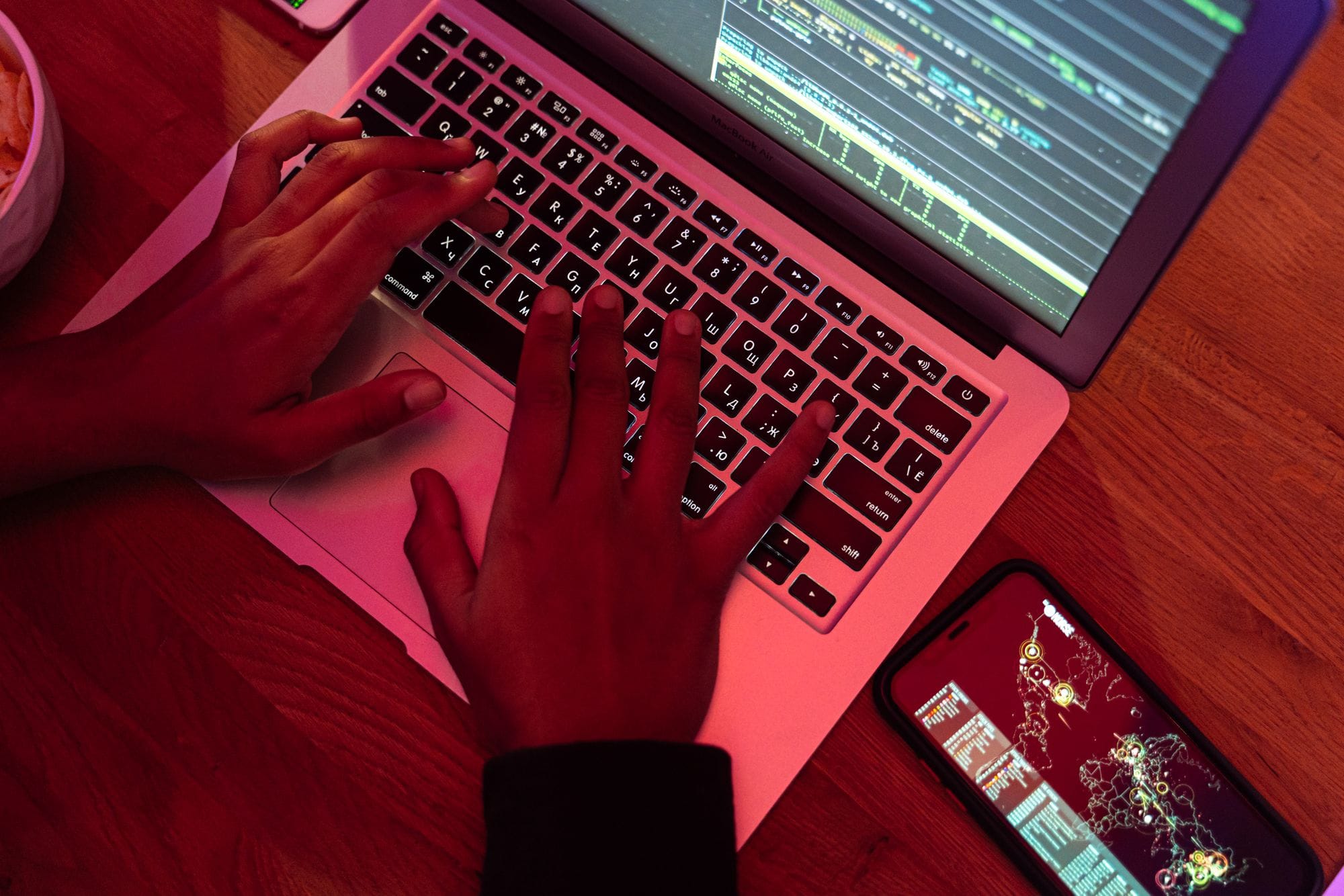 Hands typing on a laptop with code on screen, smartphone nearby at night, indoor setting.