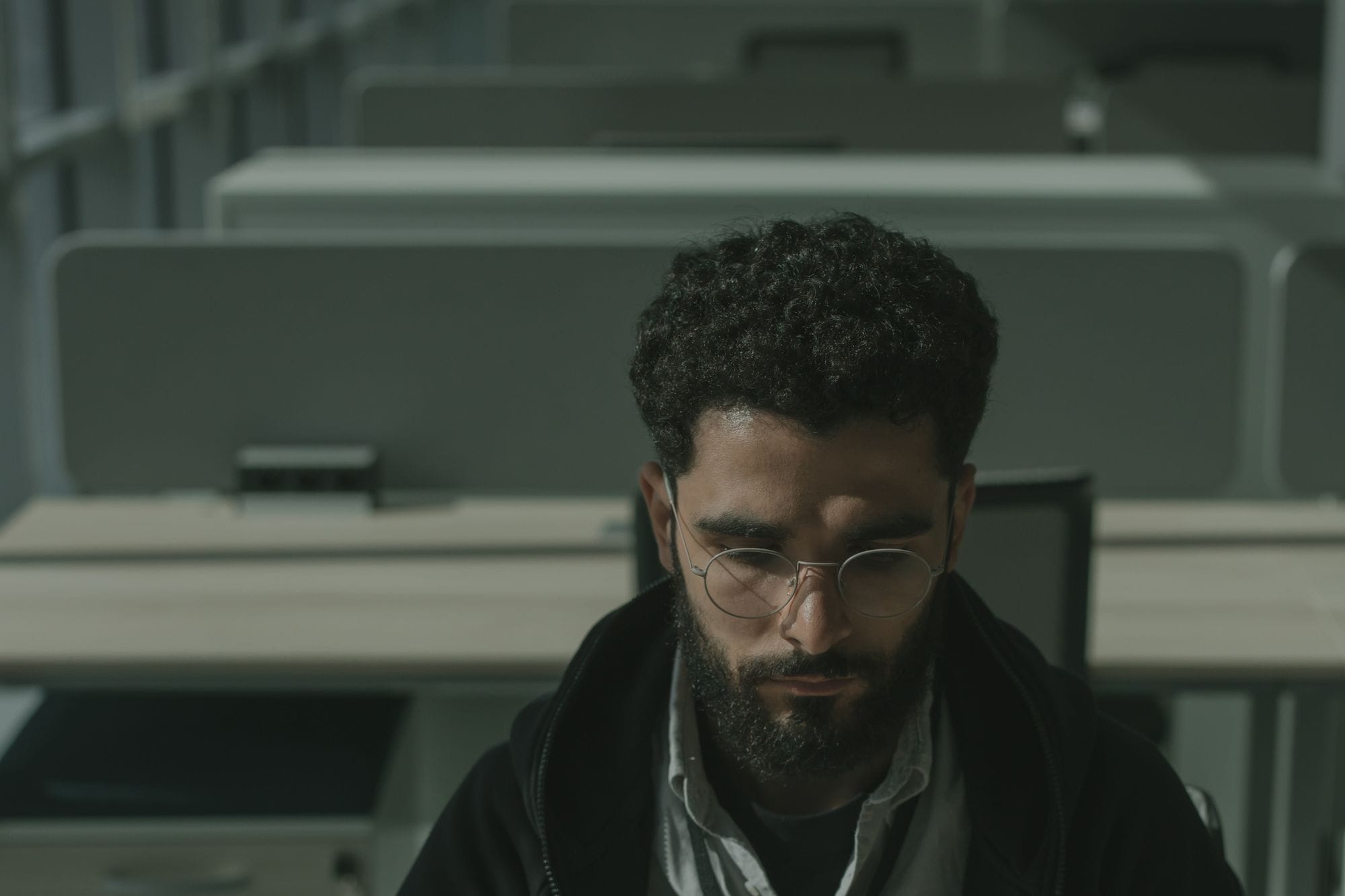 A man with eyeglasses concentrating in an empty office environment.