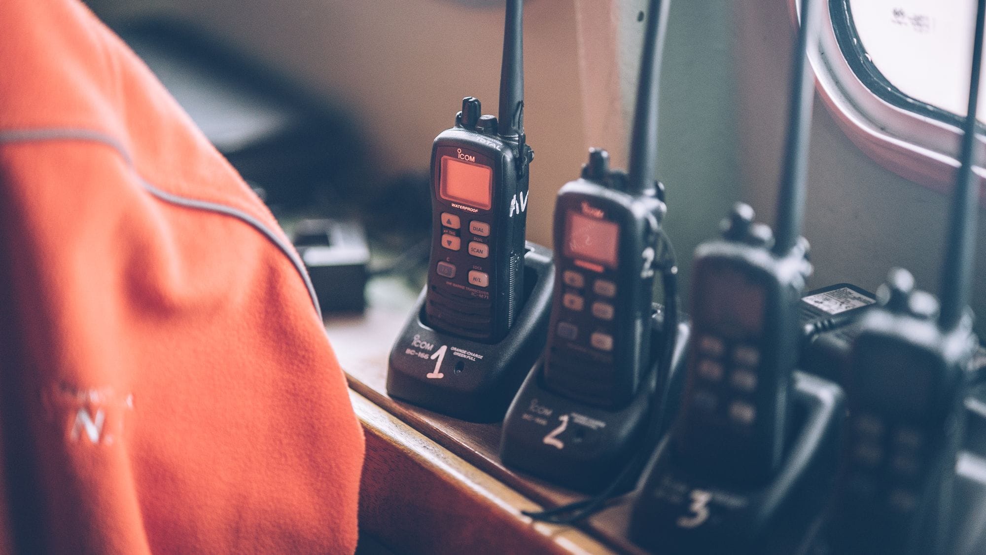 Four wireless walkie talkies in charging stations on a wooden dock indoors.