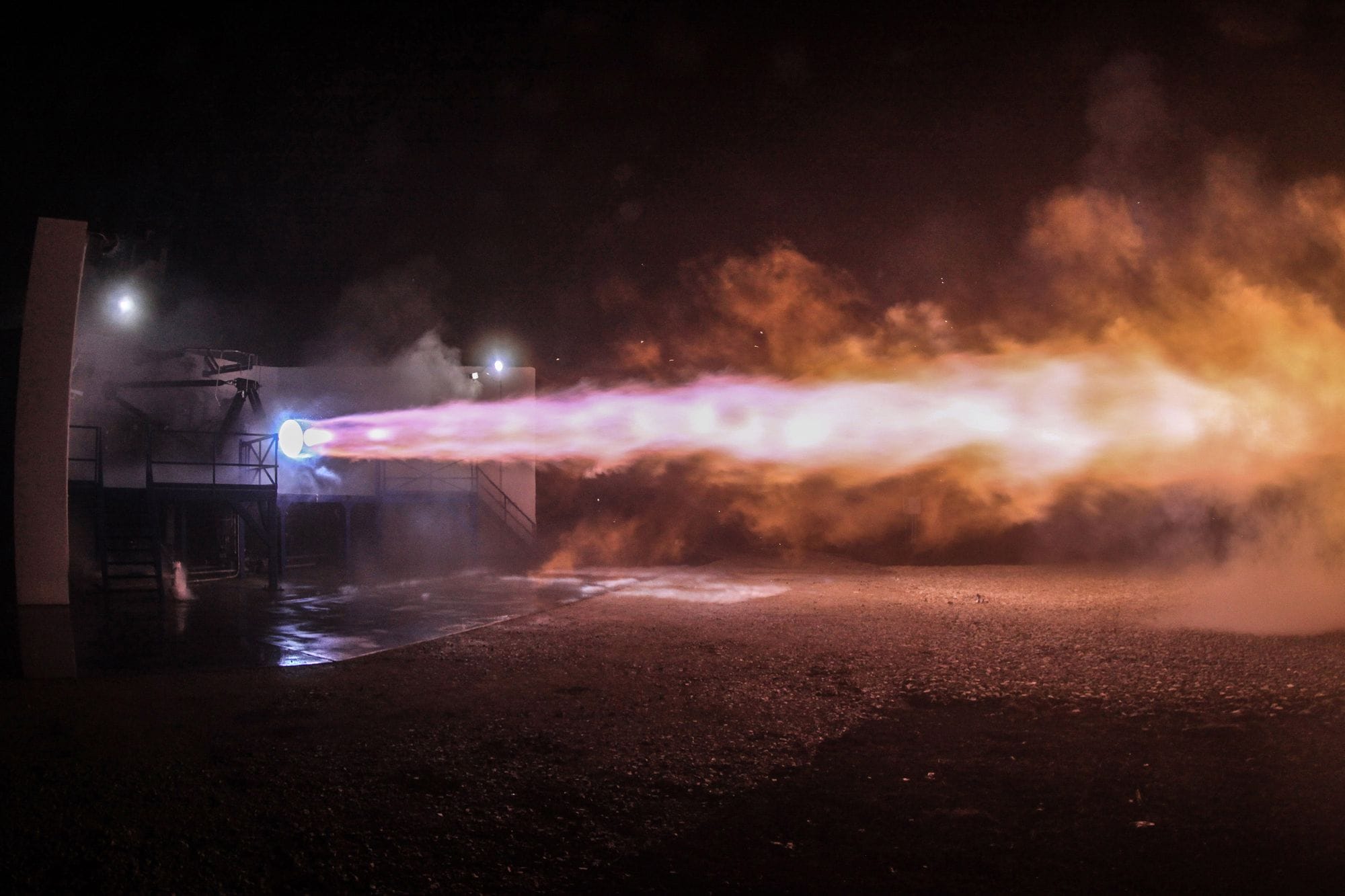 A powerful rocket engine test firing with vibrant flames illuminating the night sky.