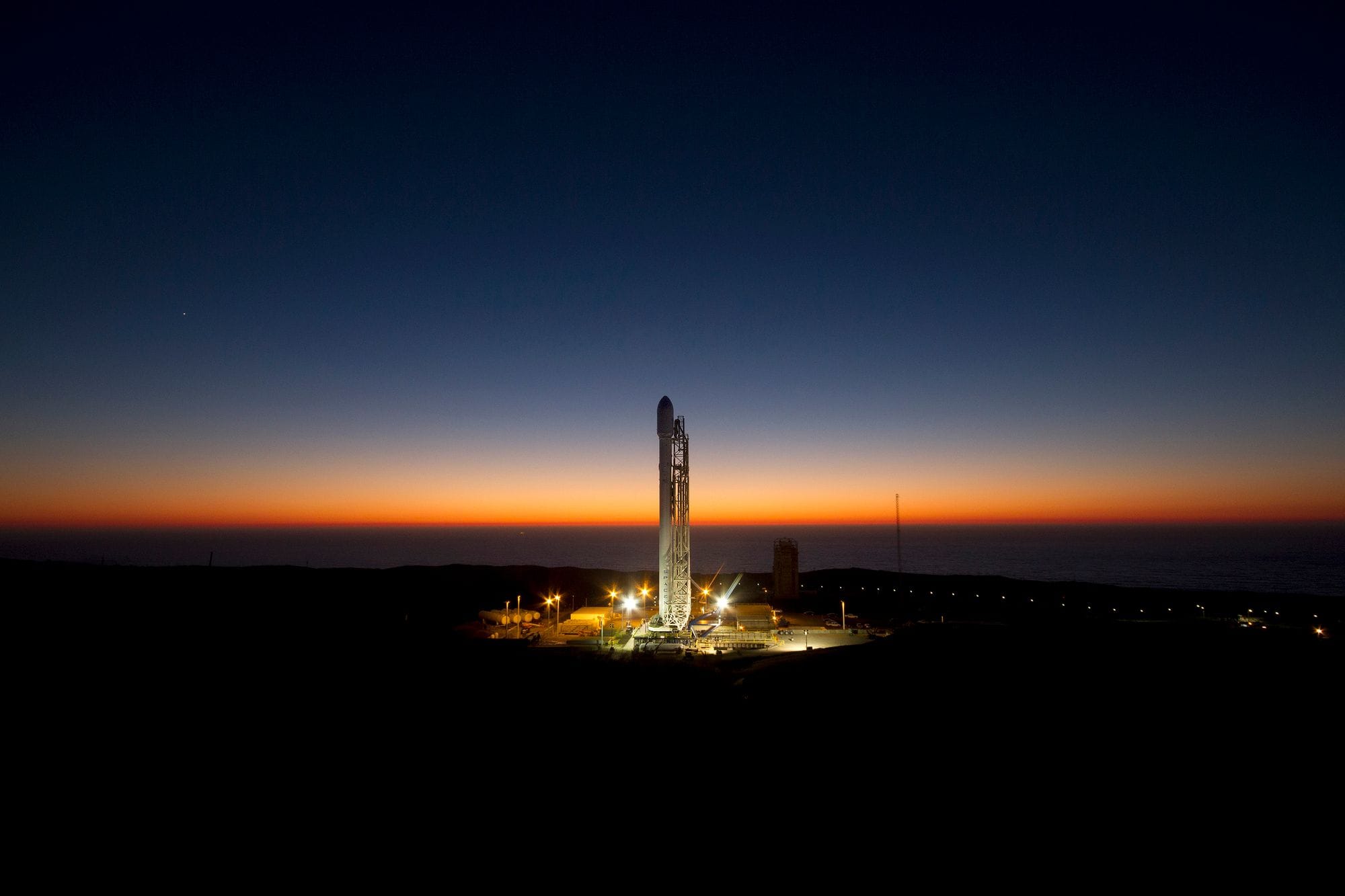A powerful rocket stands ready on its launch pad against a stunning twilight sky.