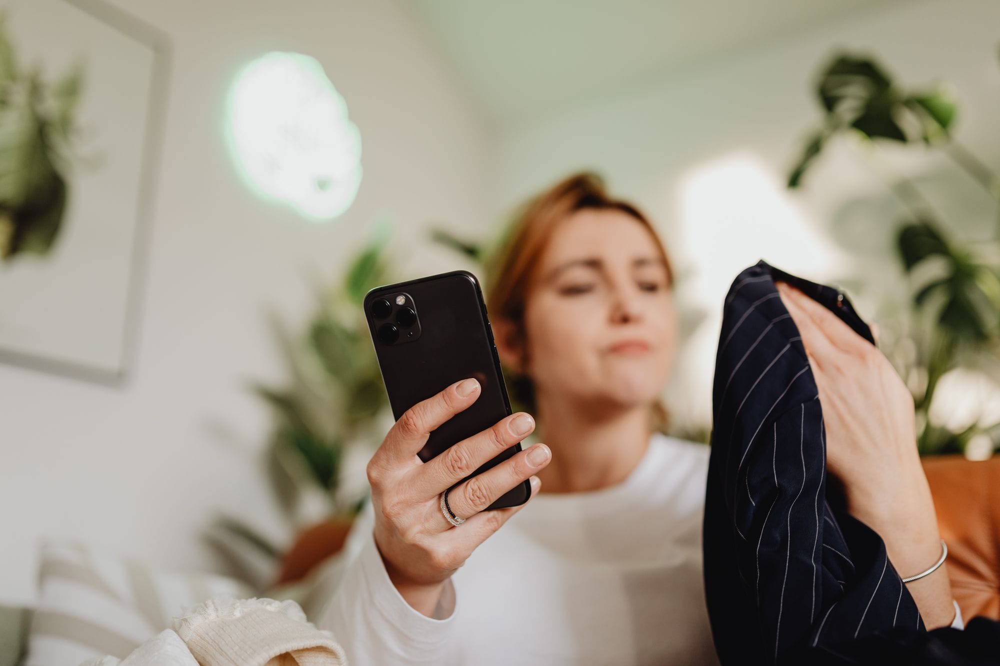 A woman uses her smartphone indoors for online shopping, holding fabric.