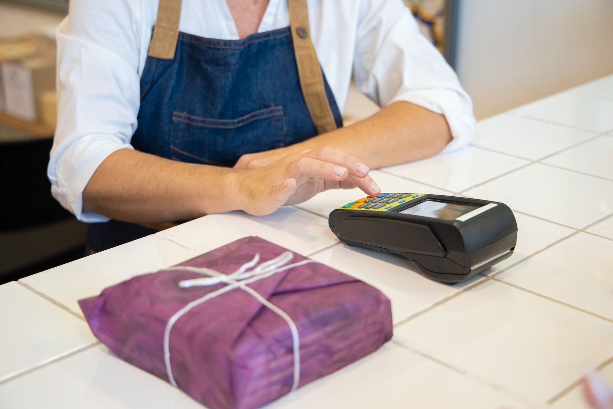 A person using contactless payment at a retail counter in Portugal wearing an apron.