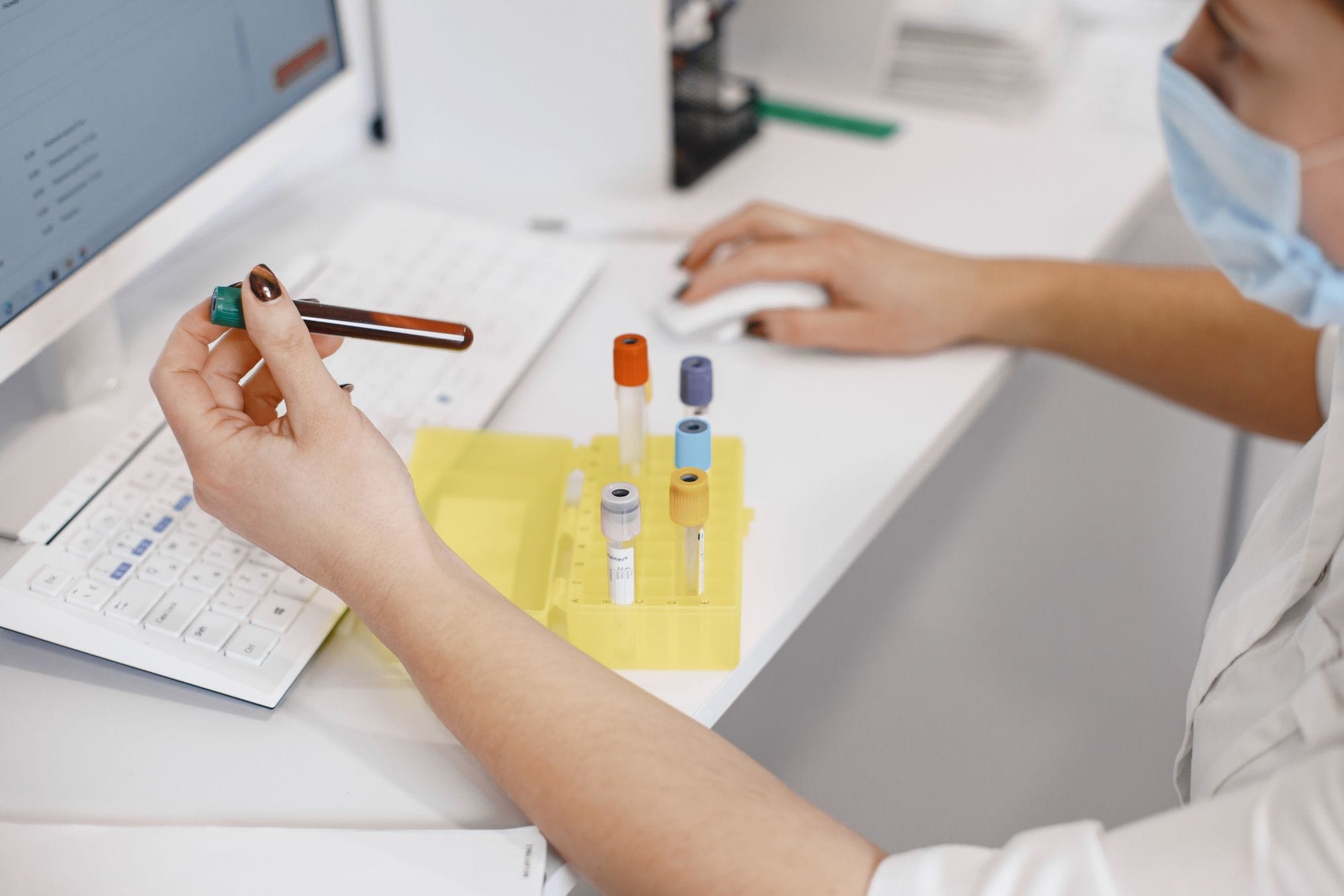 Medical worker analyzing samples at computer with test tubes nearby.