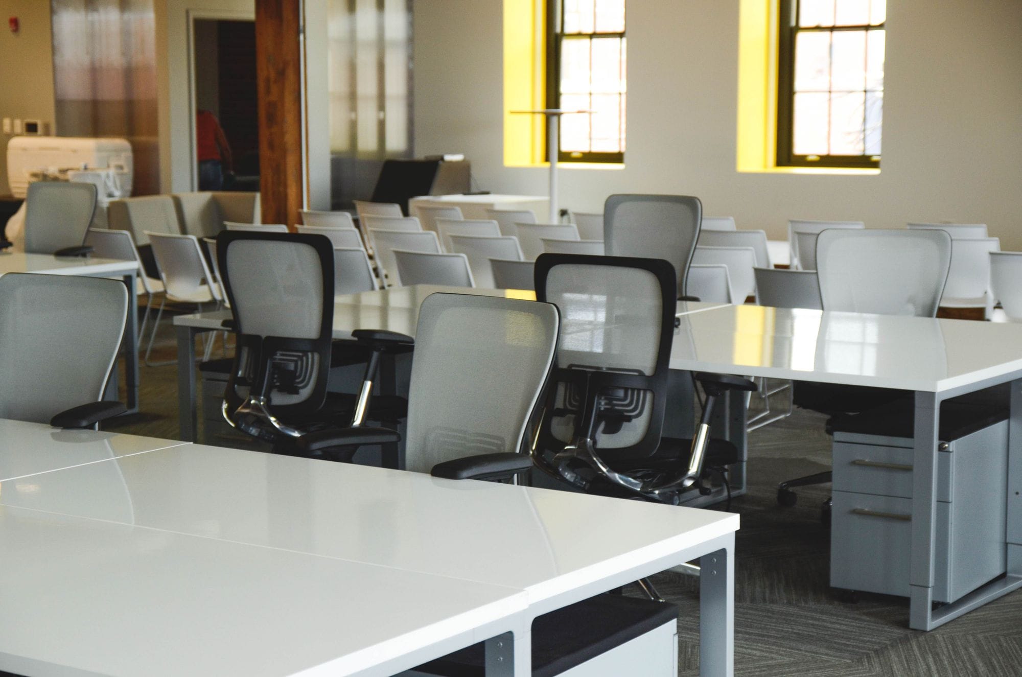 Spacious open office workspace with desks, chairs, and natural lighting.