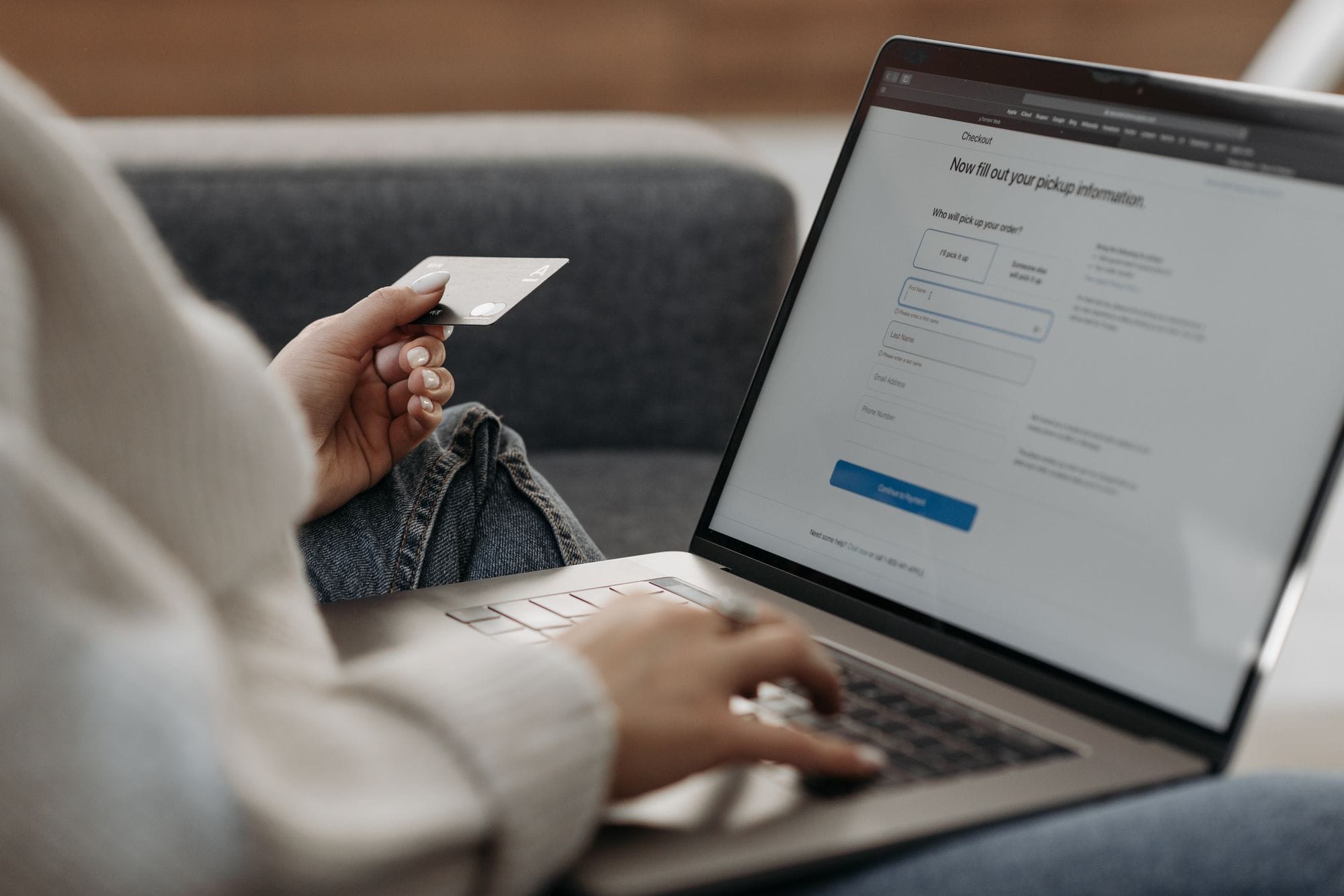 Woman holding credit card shopping online on a laptop from a couch.