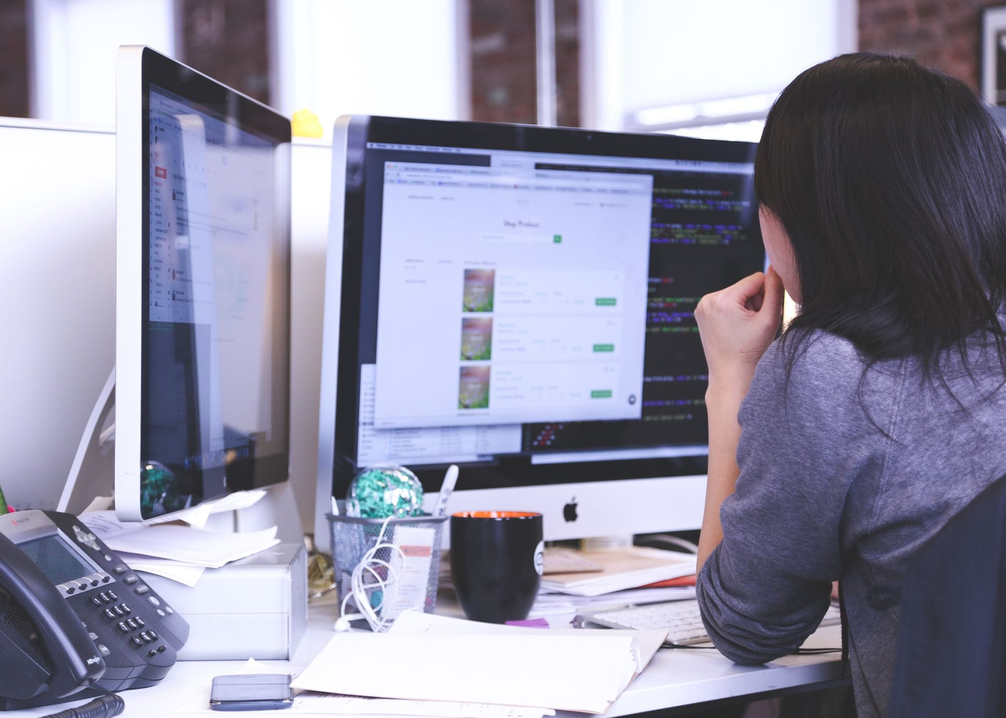 Professional woman focused on work using dual monitors in a modern office.