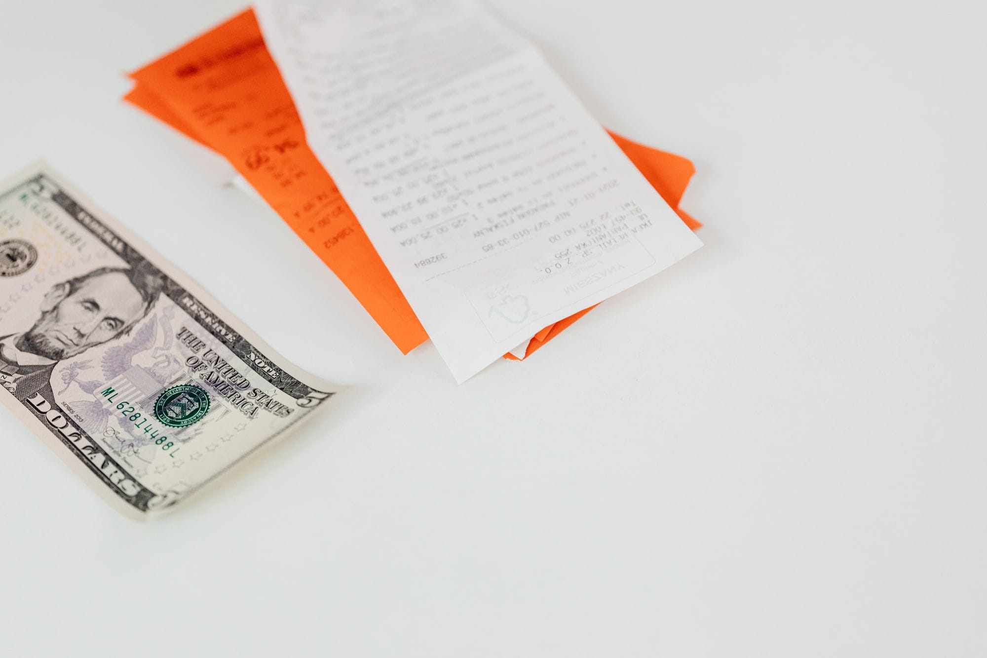 A five dollar bill and receipts on a white surface, emphasizing finance and expenses.