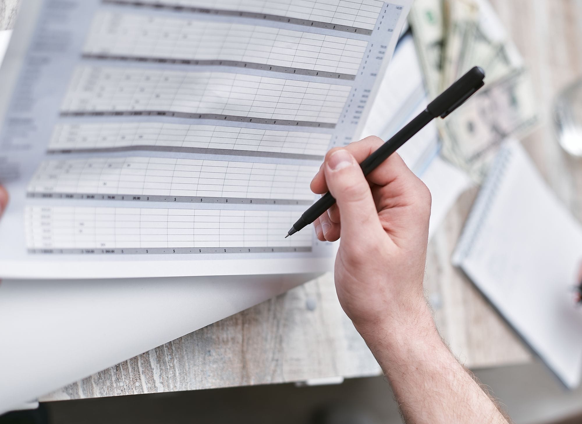 A close-up of a person holding a pen reviewing a financial document with cash visible, ideal for business themes.