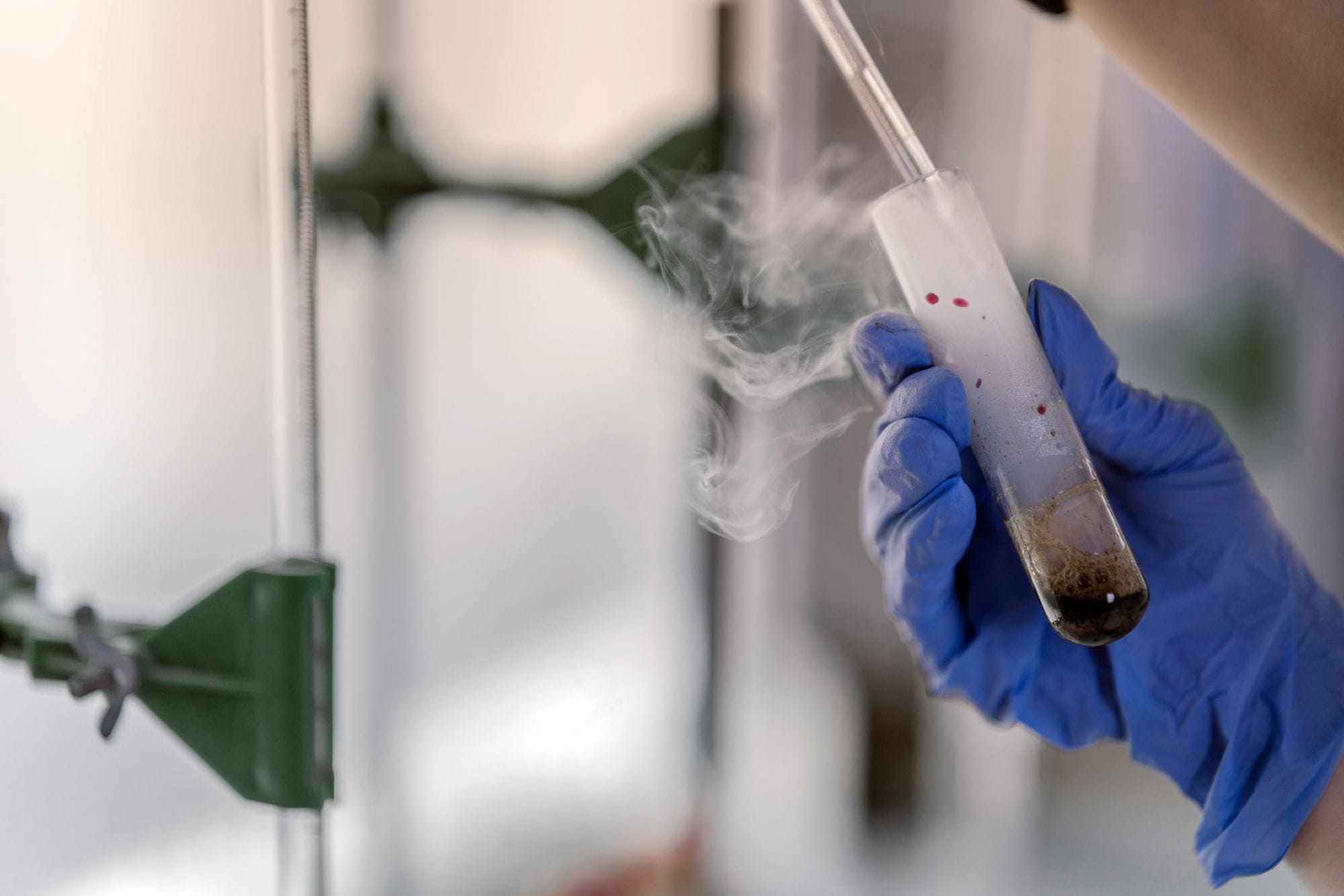 Close-up of a gloved hand holding a steaming test tube in a laboratory setting.