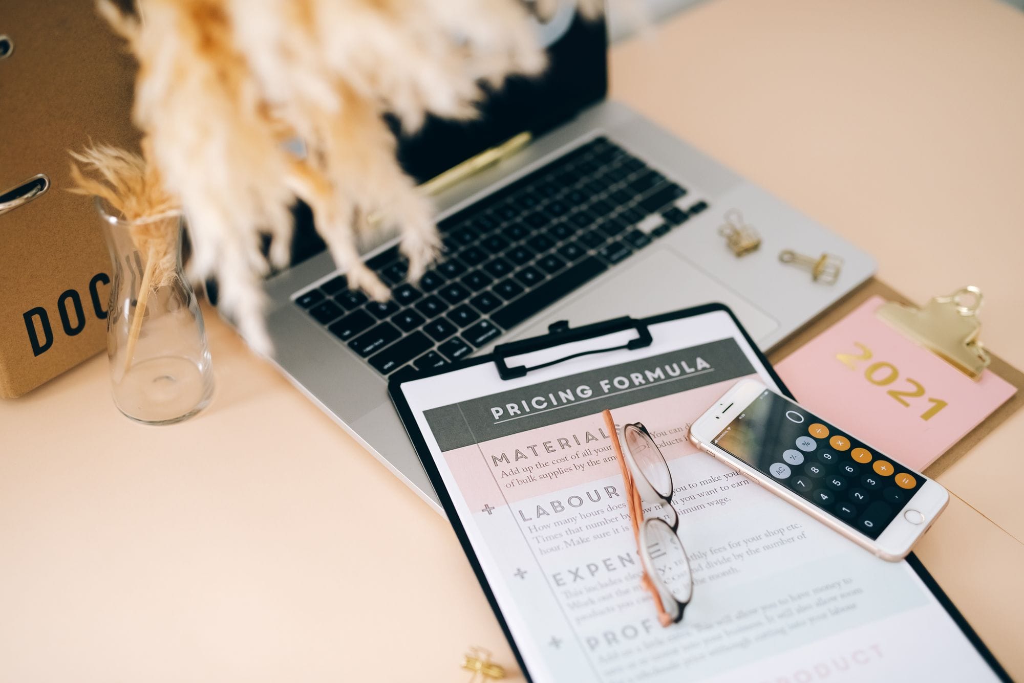 Organized office desk with pricing formula document, laptop, and smartphone calculator.