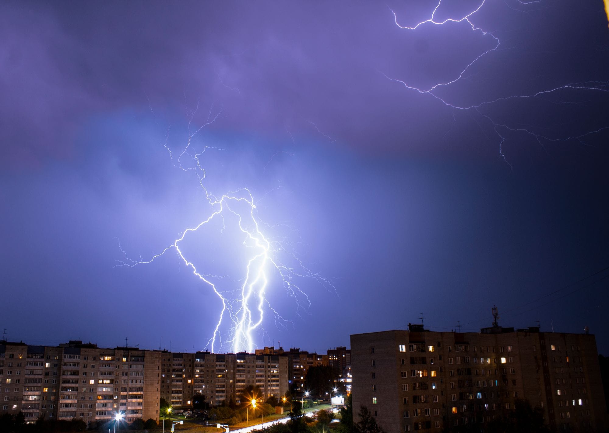 Striking lightning bolt illuminates cityscape during a nighttime thunderstorm.