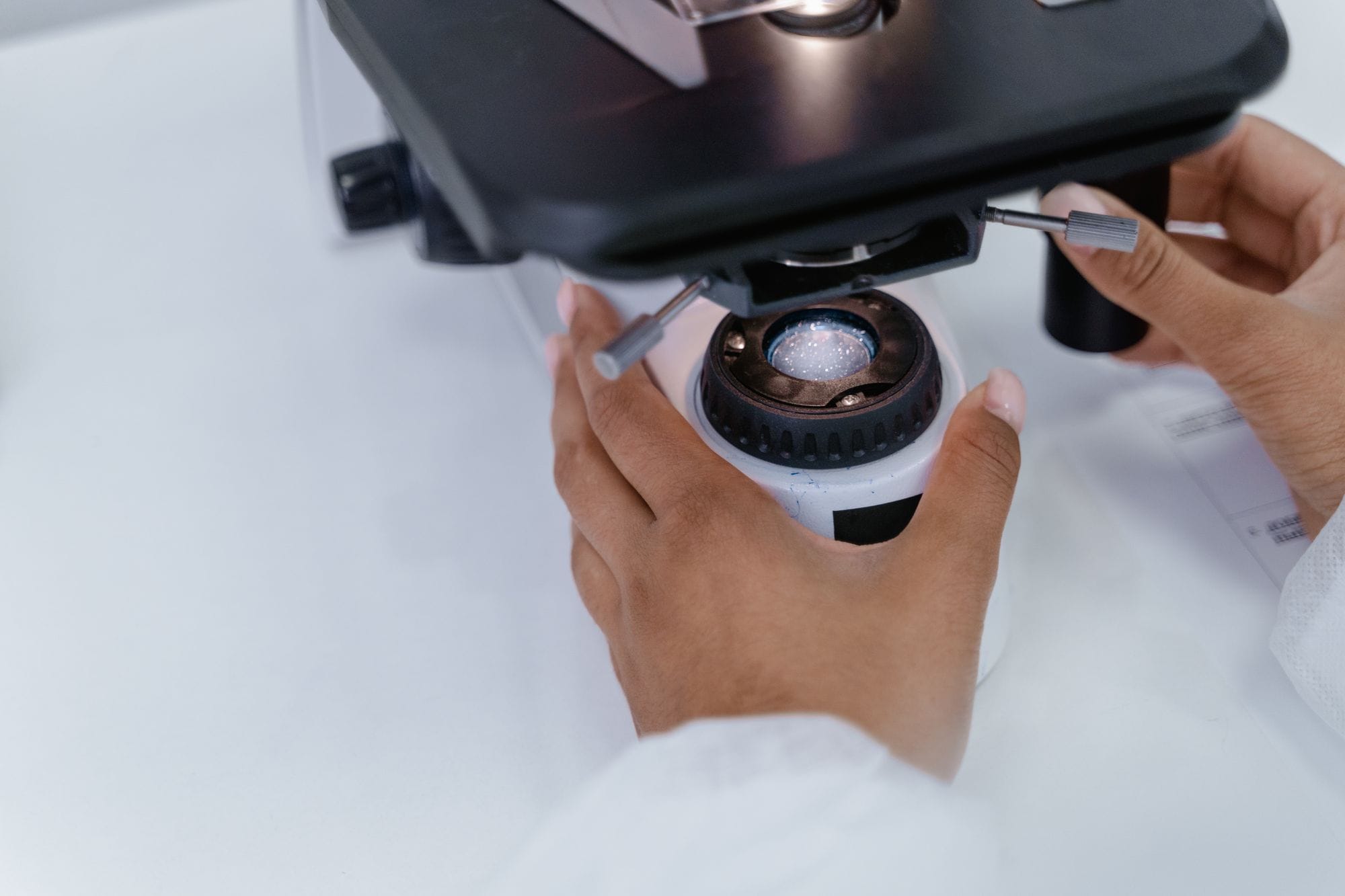 A scientist adjusts a microscope in a laboratory setting, focusing on the sample.