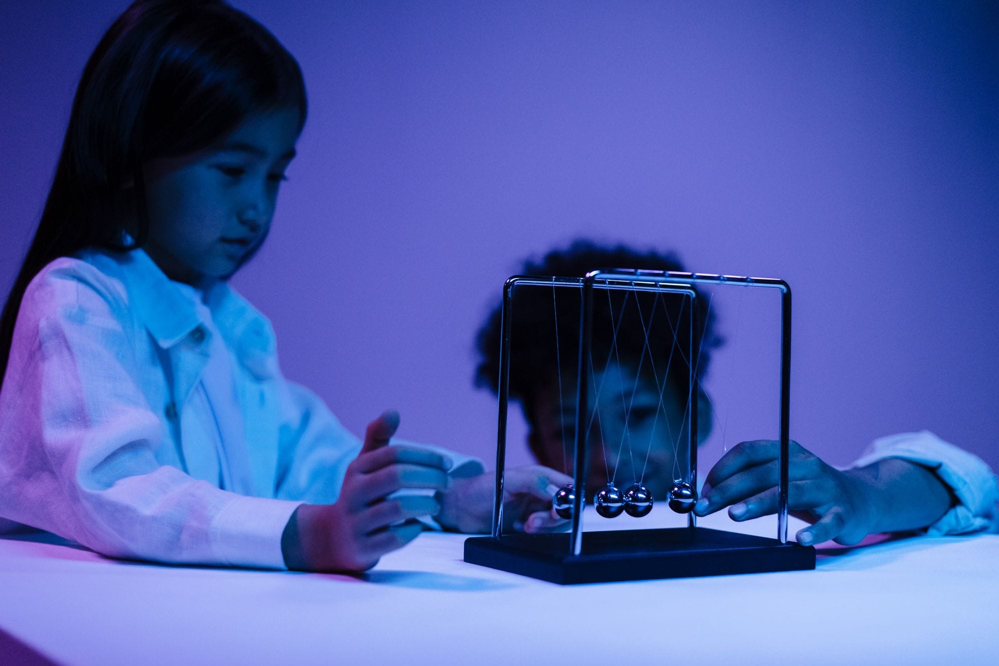 Two children focused on Newton's Cradle in vibrant studio lighting for physics learning.