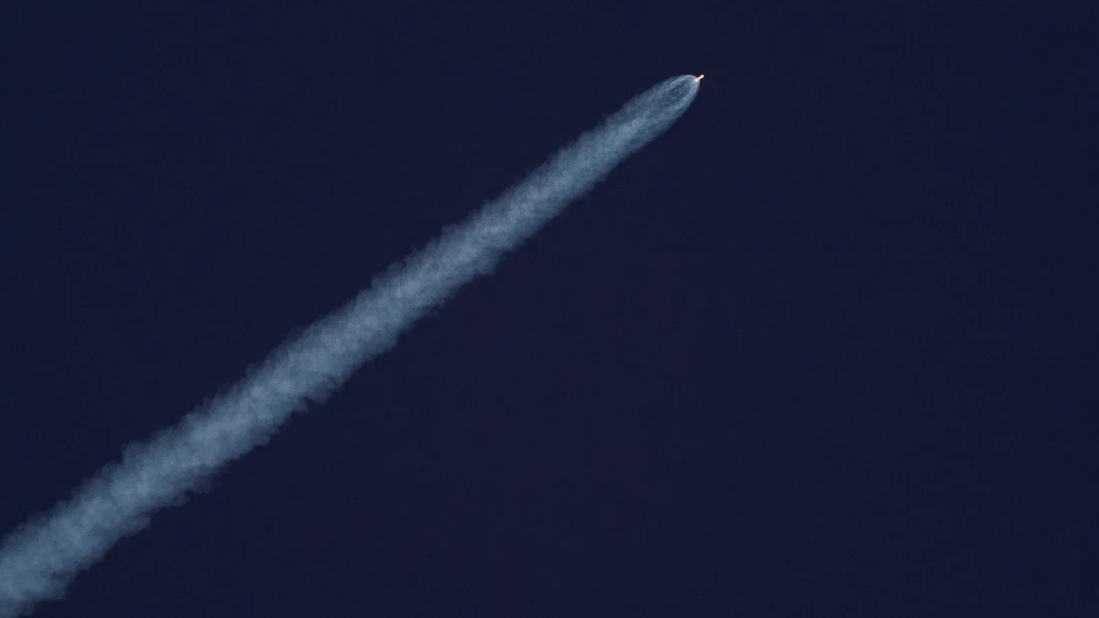 A rocket ascends into the sky, leaving a trail of smoke against the clear blue sky.