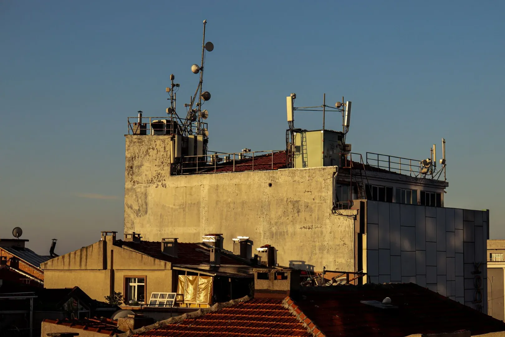A city rooftop with antennas and relay towers against a clear blue sky at sunset.