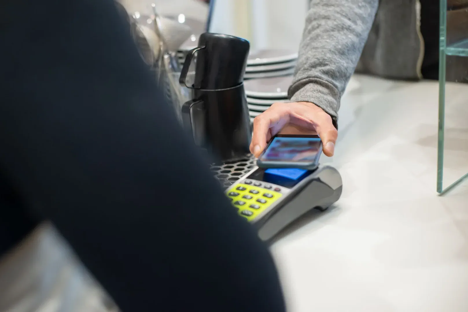 A customer makes a contactless payment using a smartphone at a café, showcasing modern digital transactions.