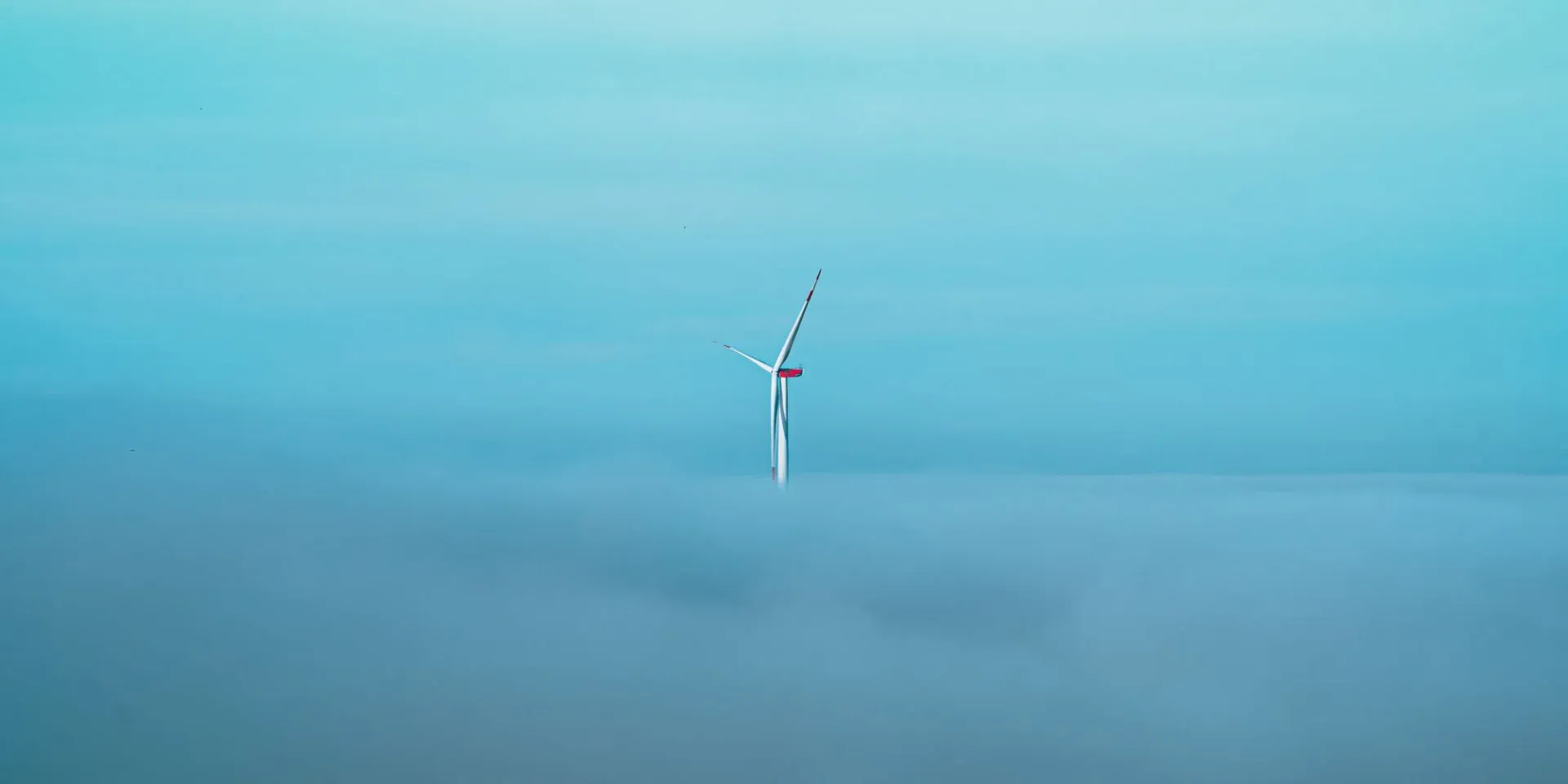 A lone wind turbine pierces through a dense fog, set against a clear blue sky, symbolizing sustainable energy.